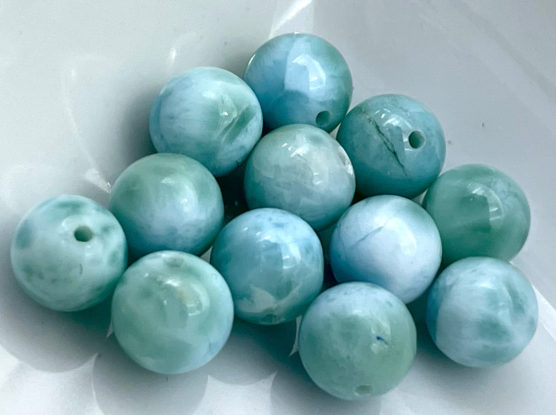Round light blue and white larimar  beads strung on a blue cord, photographed close-up against a plain white background.