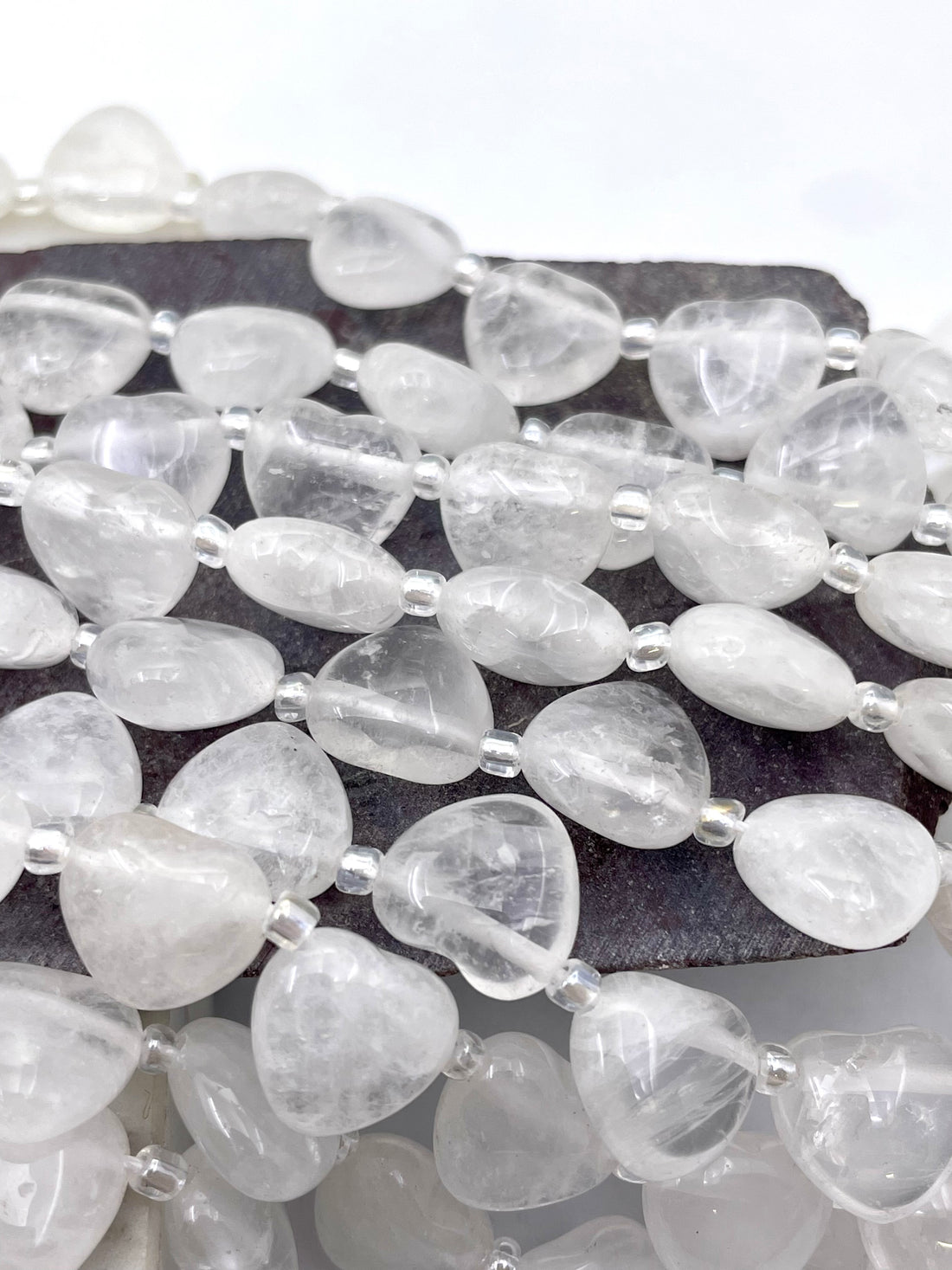 Multiple strands of polished gemstone heart-shaped gemstone beads arranged vertically, showing a variety of colors and stone types including pink, blue, green, yellow, black, and white.