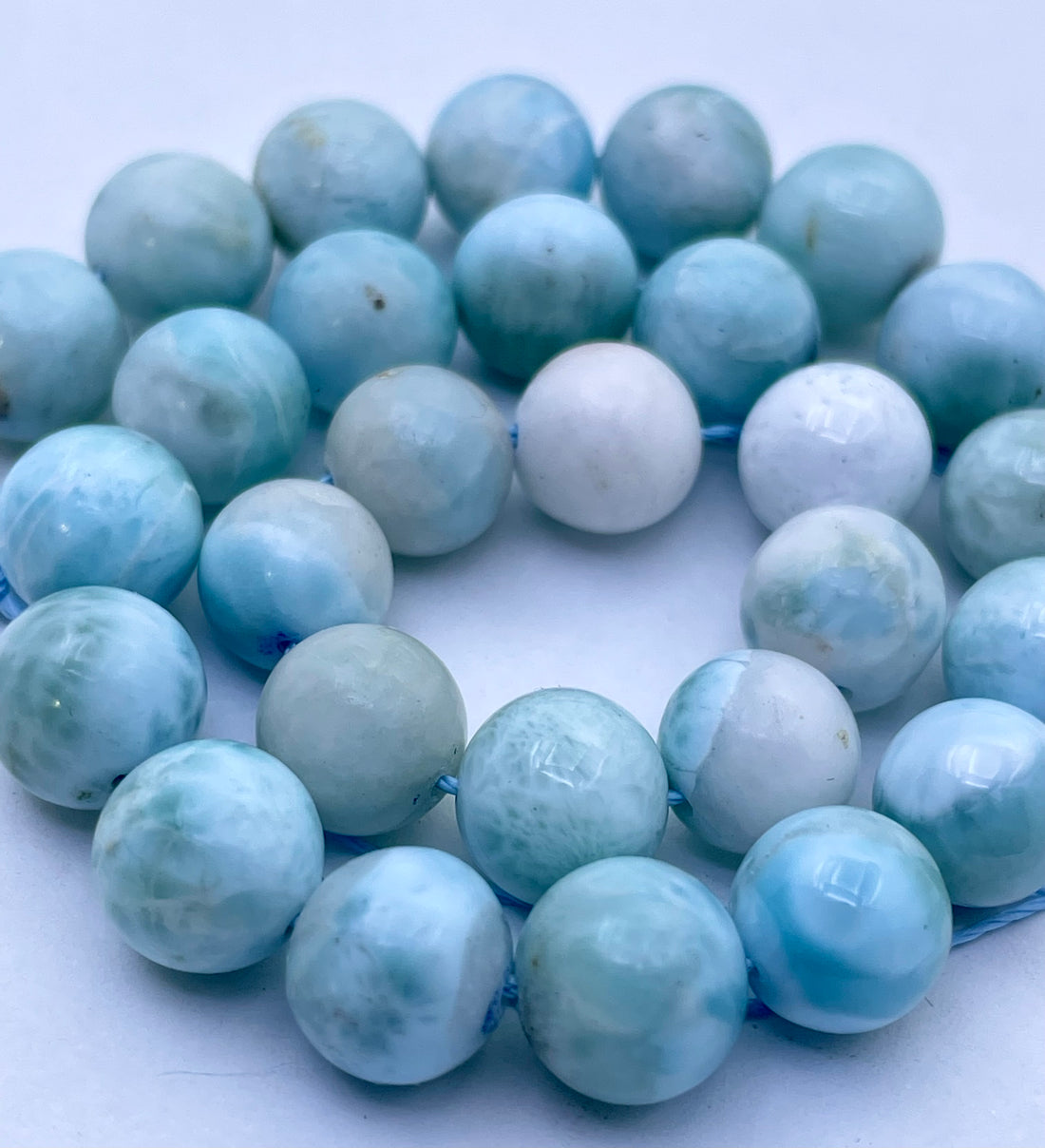 Round light blue and white larimar  beads strung on a blue cord, photographed close-up against a plain white background.