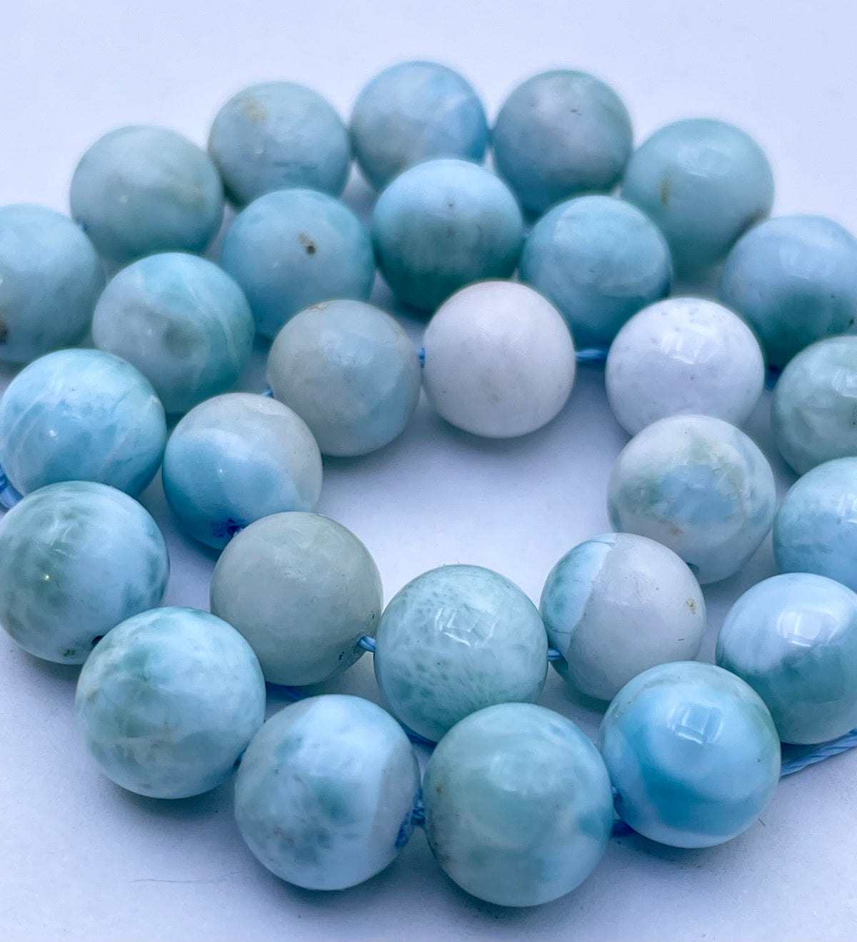 Round light blue and white larimar  beads strung on a blue cord, photographed close-up against a plain white background.