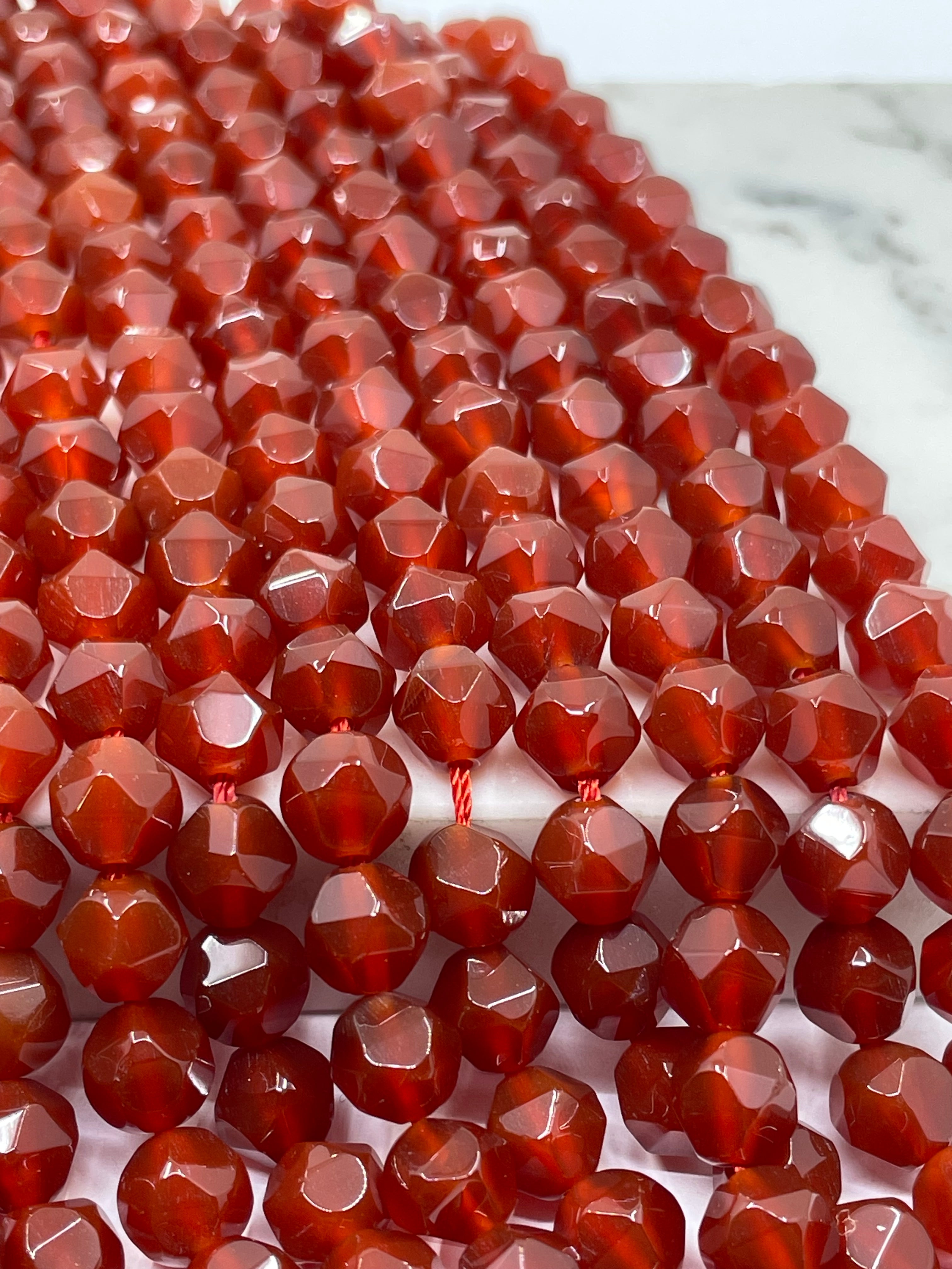 Faceted carnelian beads in a translucent reddish-brown color, strung together on a cord against a light marble-like background.