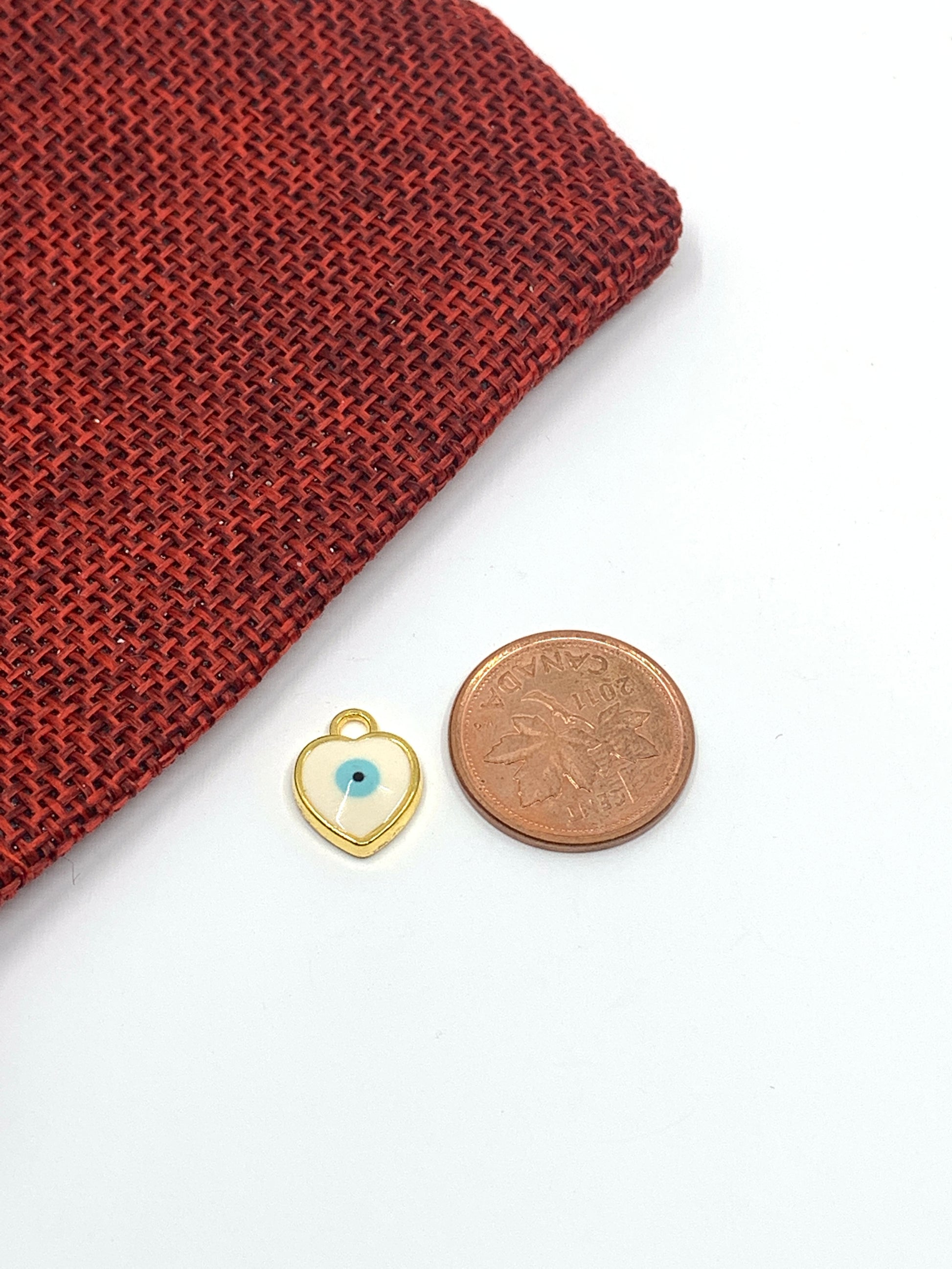 Comparison of white heart evil eye charm with a coin for size reference