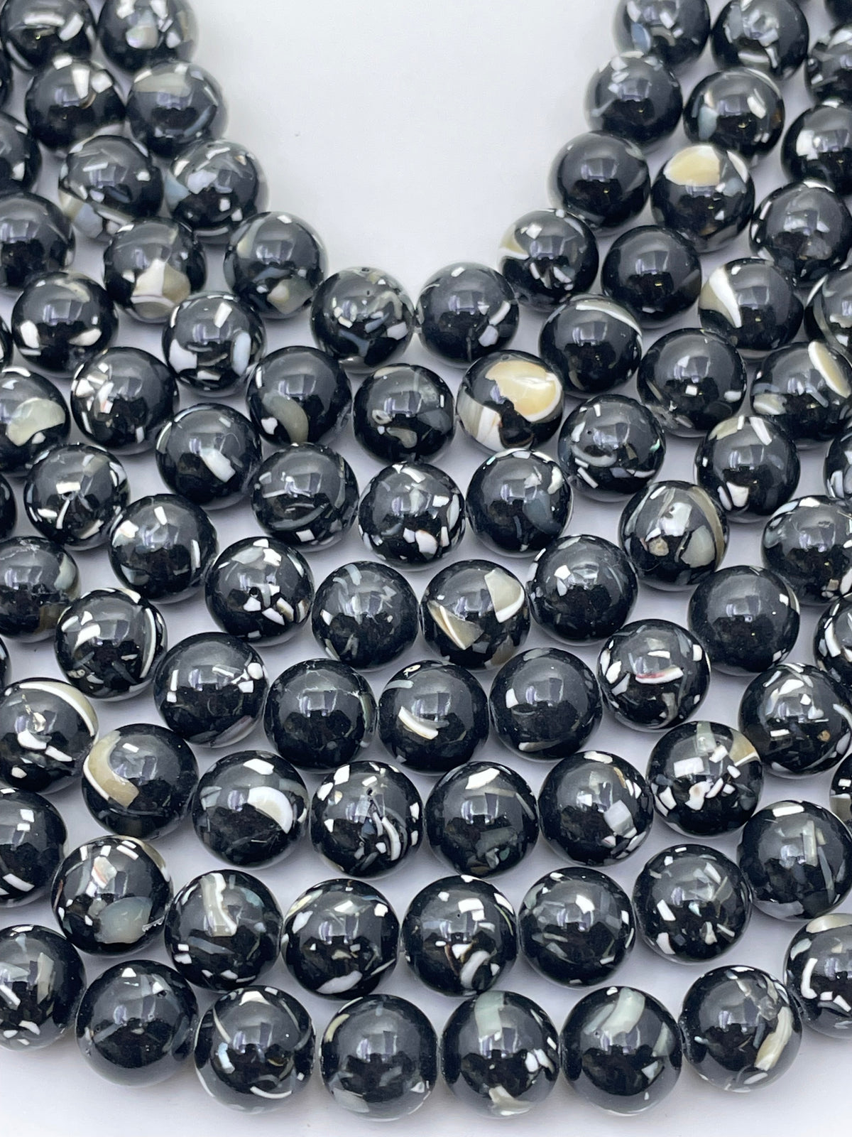 Multiple strands of  black mop beads with natural white and gray marbled patterns, arranged on a plain white background.