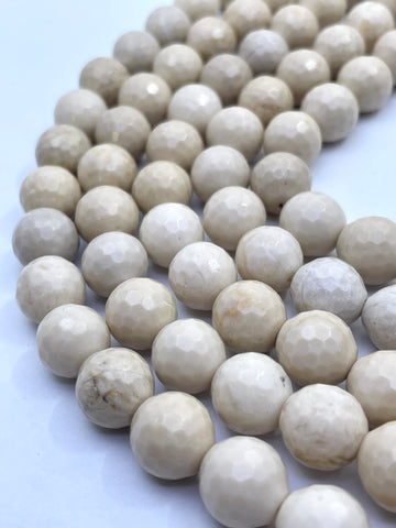 Faceted round riverstone/ fossil stone beads in a warm cream or ivory tone, arranged in curved rows on a plain light background.