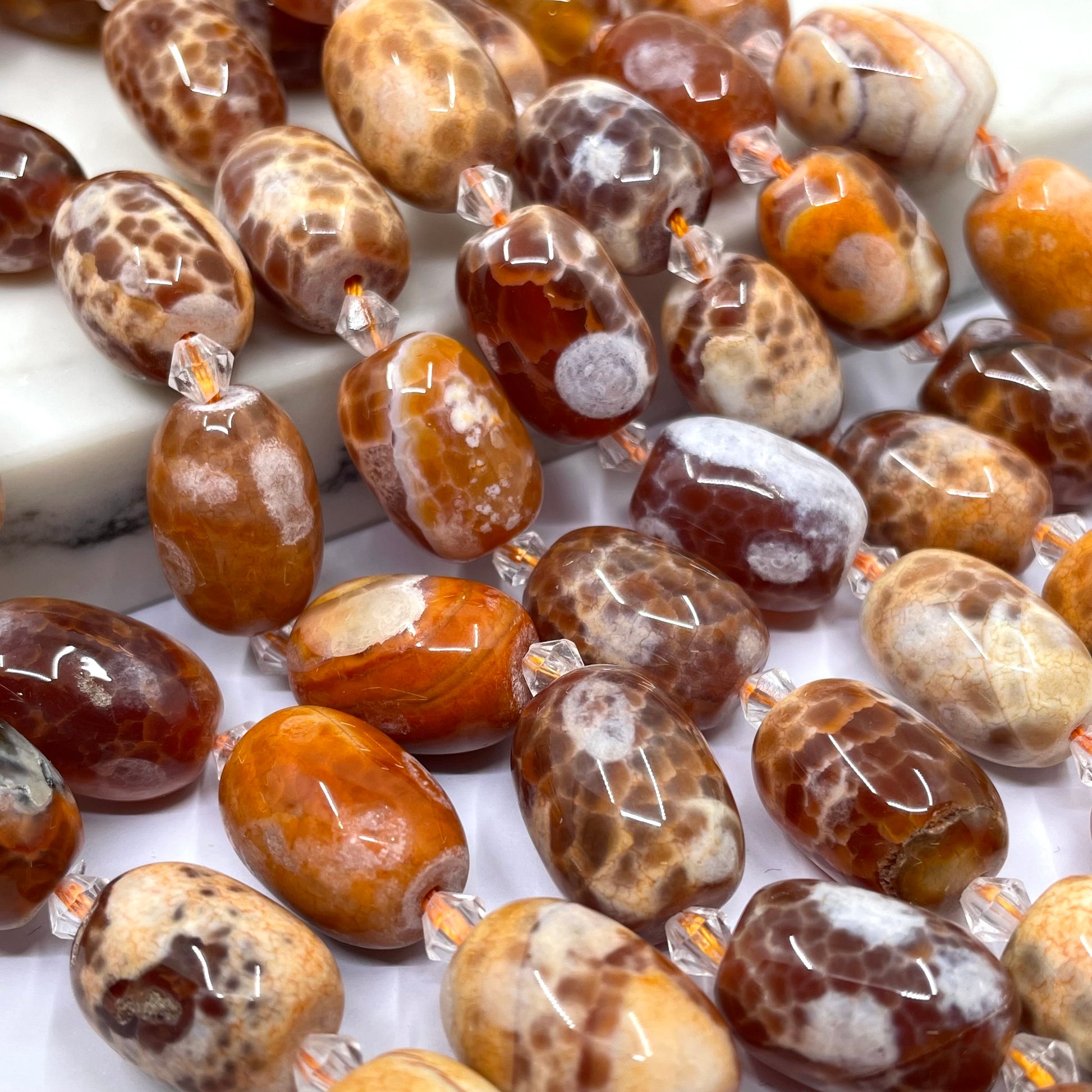 Close-up of glossy oval gemstone beads with mottled brown, cream, and orange patterns, threaded on clear cords.