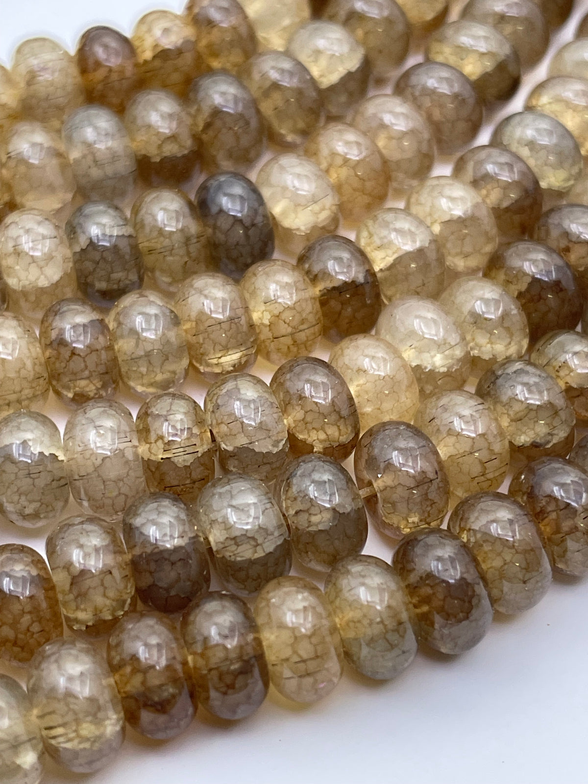 Close-up of smooth donut oval glass beads in a smoky amber-brown translucent stone, arranged in curved rows on a white background.