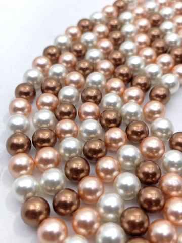 Multiple strands of shell pearl beads in a mix of metallic rose gold, champagne gold, and white, arranged in a curved pattern on a white background.
