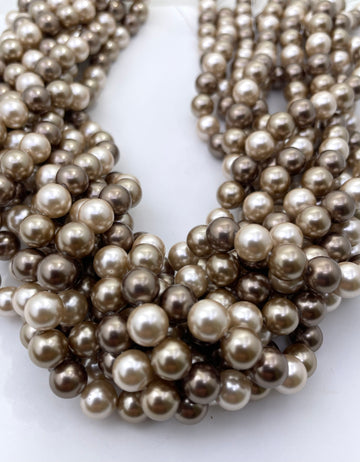Multiple strands of round shell pearl beads in a champagne to taupe-gray color, arranged in a curved cluster on a plain white background.