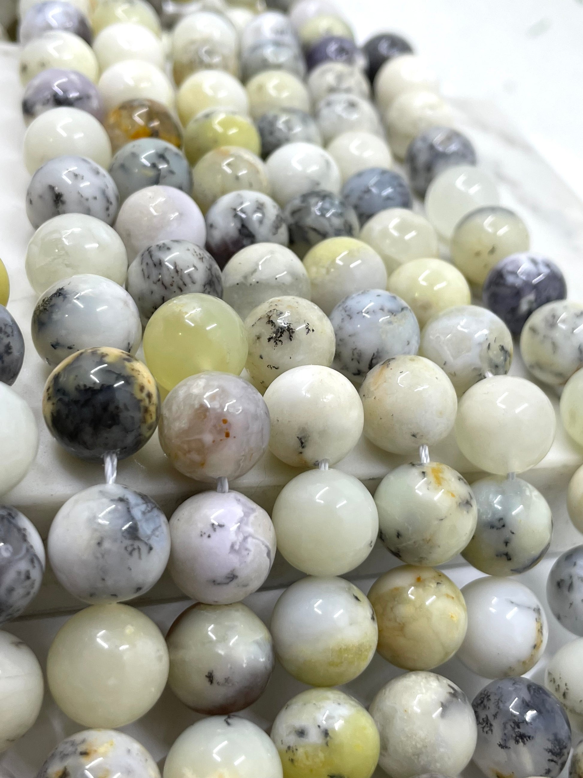 Close-up of multiple strands of polished round gemstone beads in soft white, cream, pale yellow, gray, and black marbled patterns.