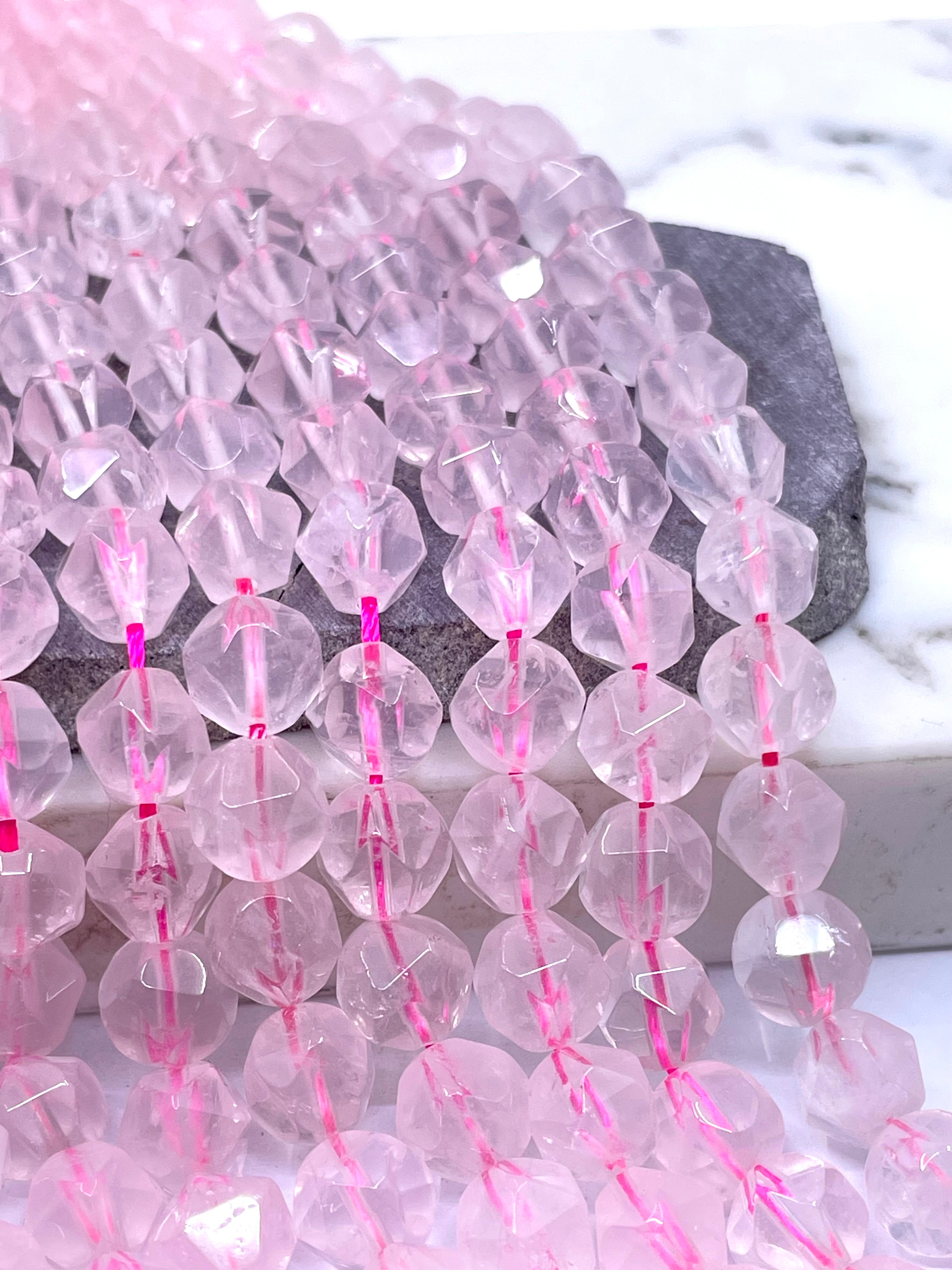 Faceted rose quartz beads strung on pink thread, draped over a dark stone and white marble surface.