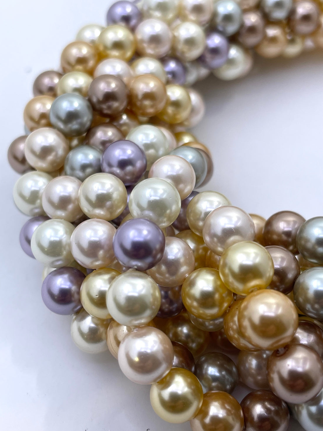 Close-up of strands of shell pearl beads in a mix of champagne gold, cream, white, taupe, and lavender purple on a white background.