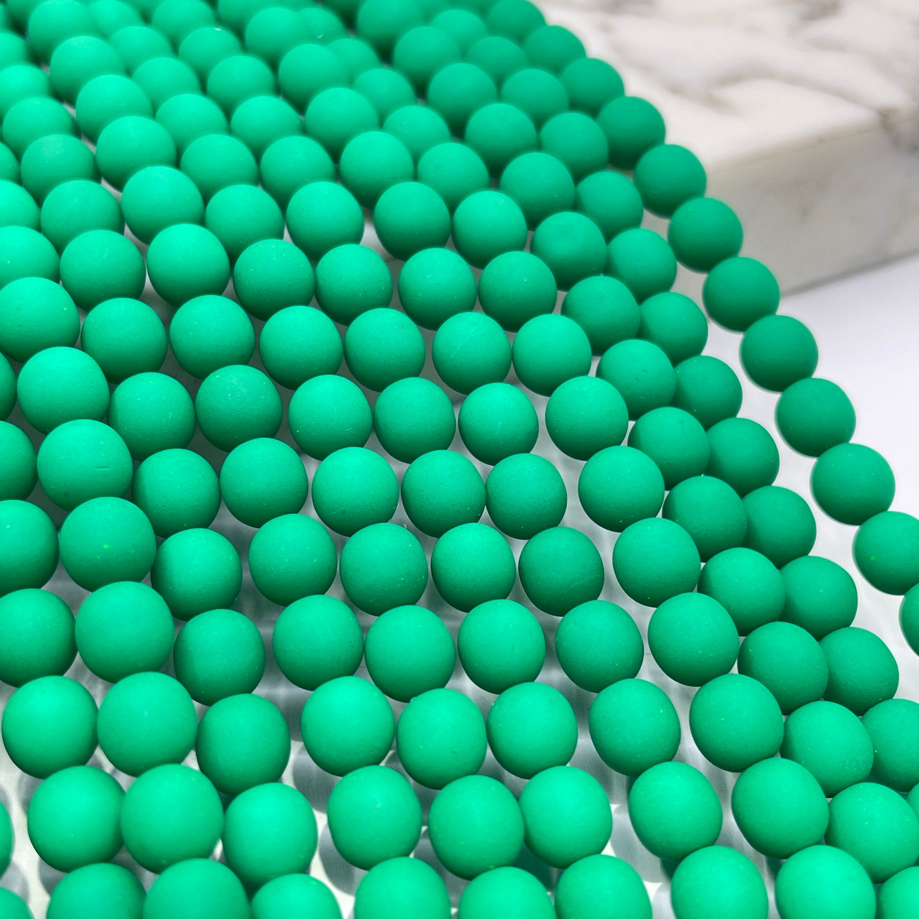 Green matte round beads arranged in parallel rows on a white surface with a blurred marble block in the background.