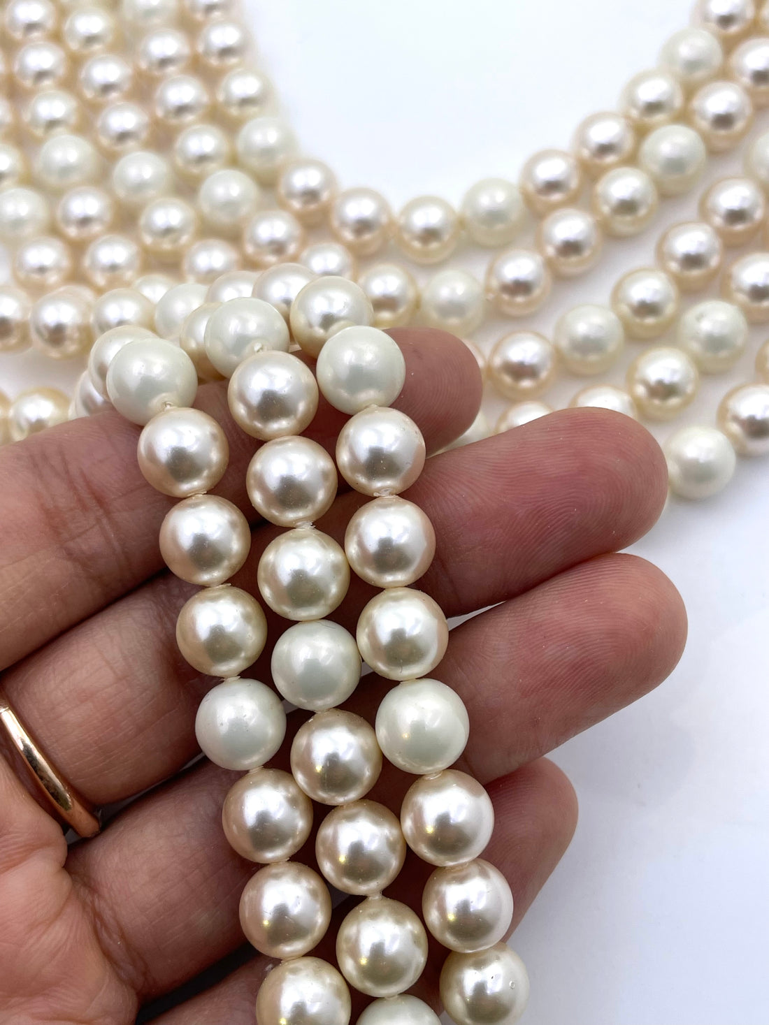 Multiple strands of round shell pearl beads in an off-white, creamy color, arranged in parallel rows on a plain white background.
