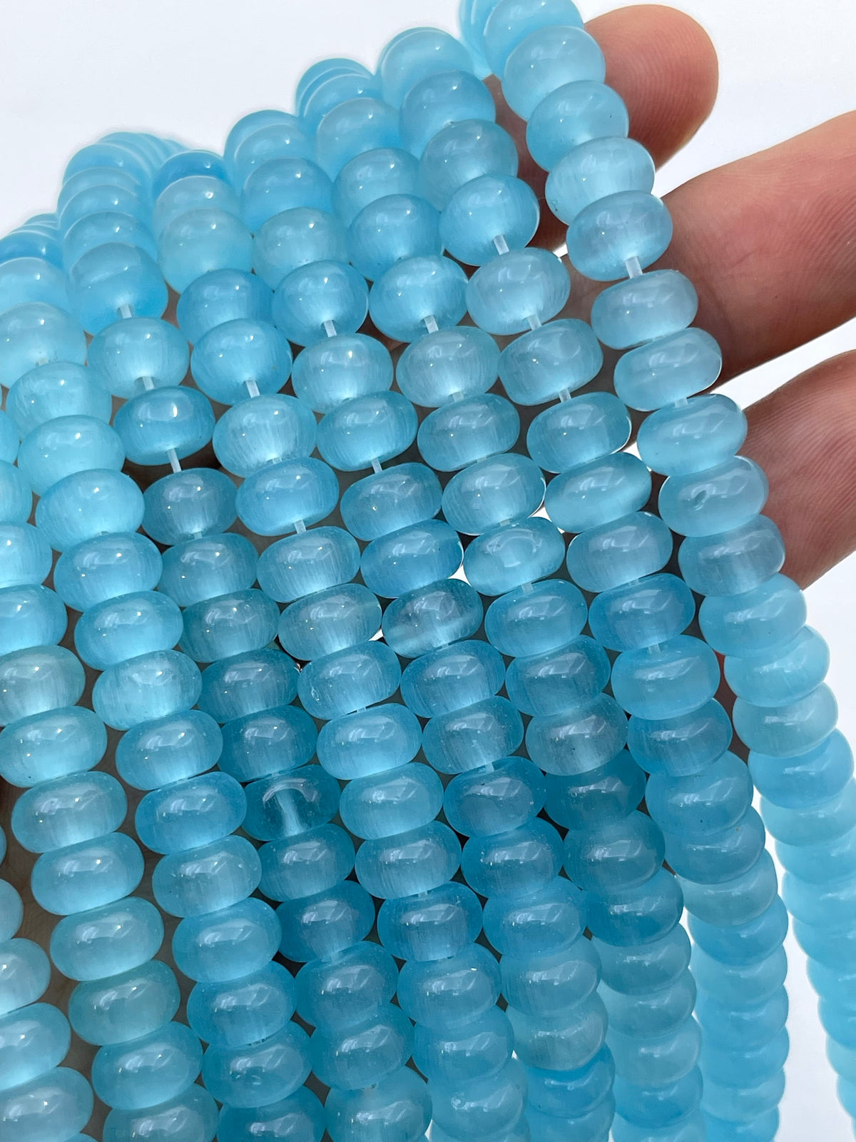 Light blue cats eye translucent donut gemstone beads strung on cords, held in a hand against a white background.
