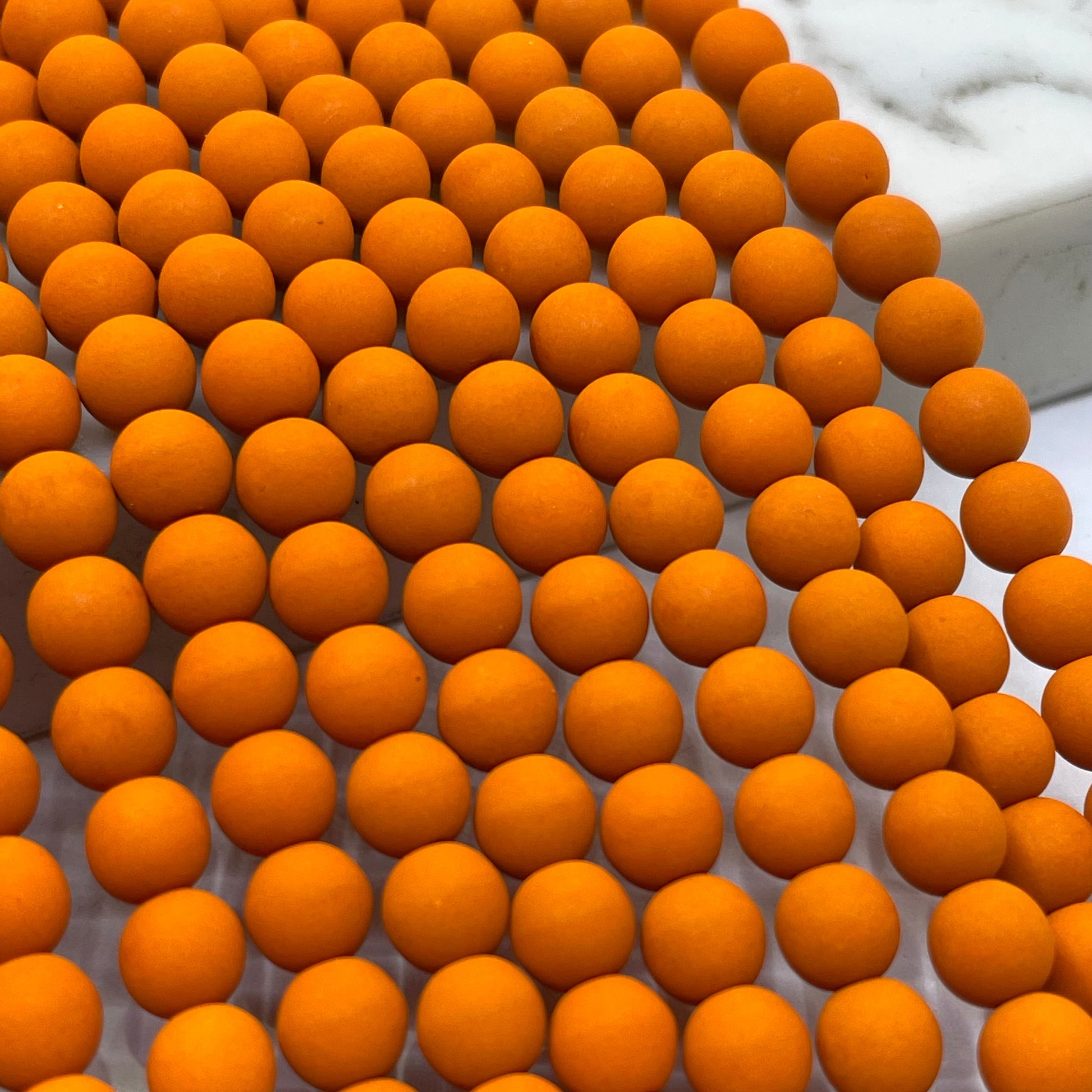A close-up of velvet rust orange beads arranged in rows on a white marble surface.