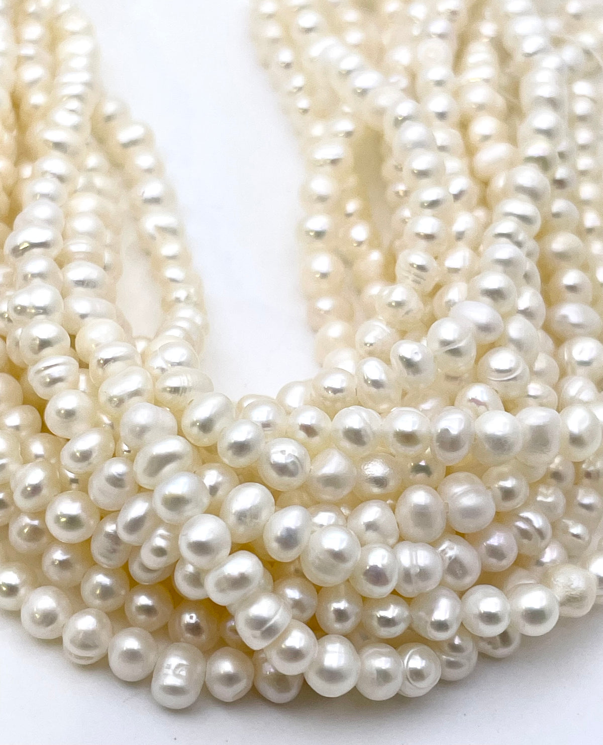 Multiple strands of potato white freshwater pearls arranged in soft curves on a plain white background.