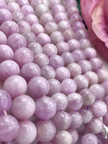 Close-up of many polished round kunzite beads in a soft lavender-pink color, arranged tightly together with a pink flower partially visible at the upper right.