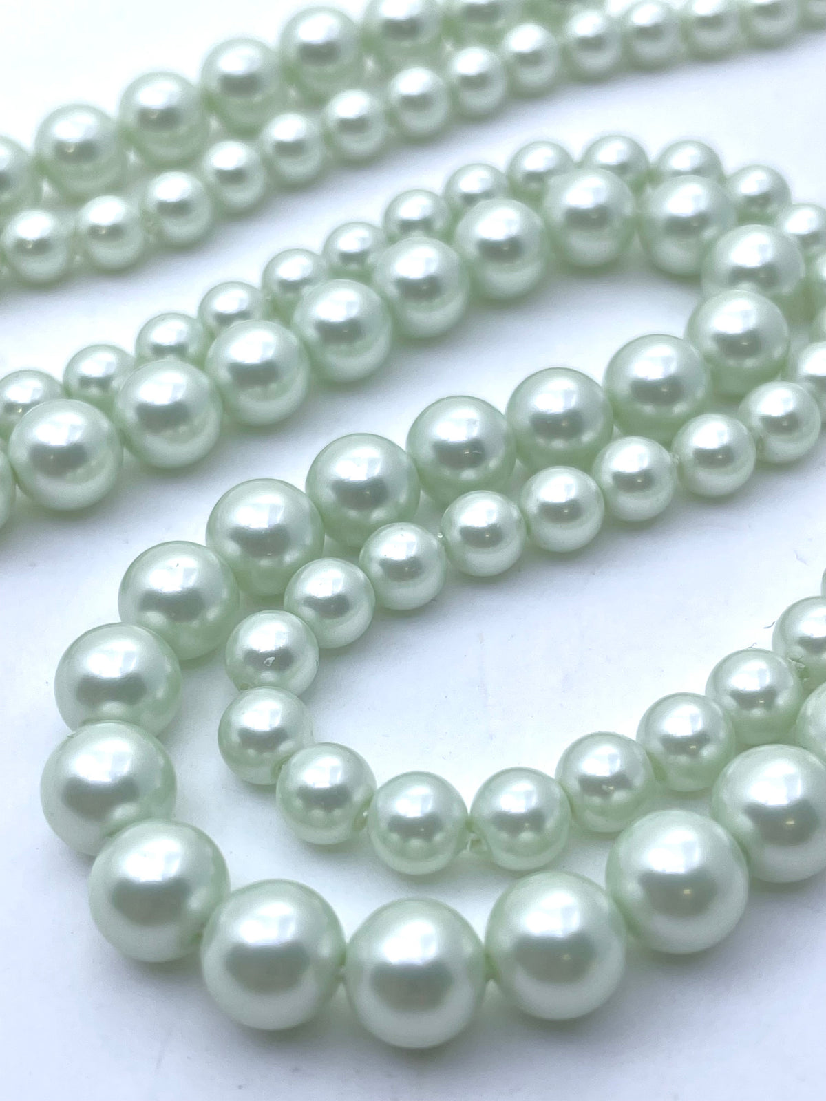 Multiple strands of light green shell pearl beads arranged in loops on a plain white background.