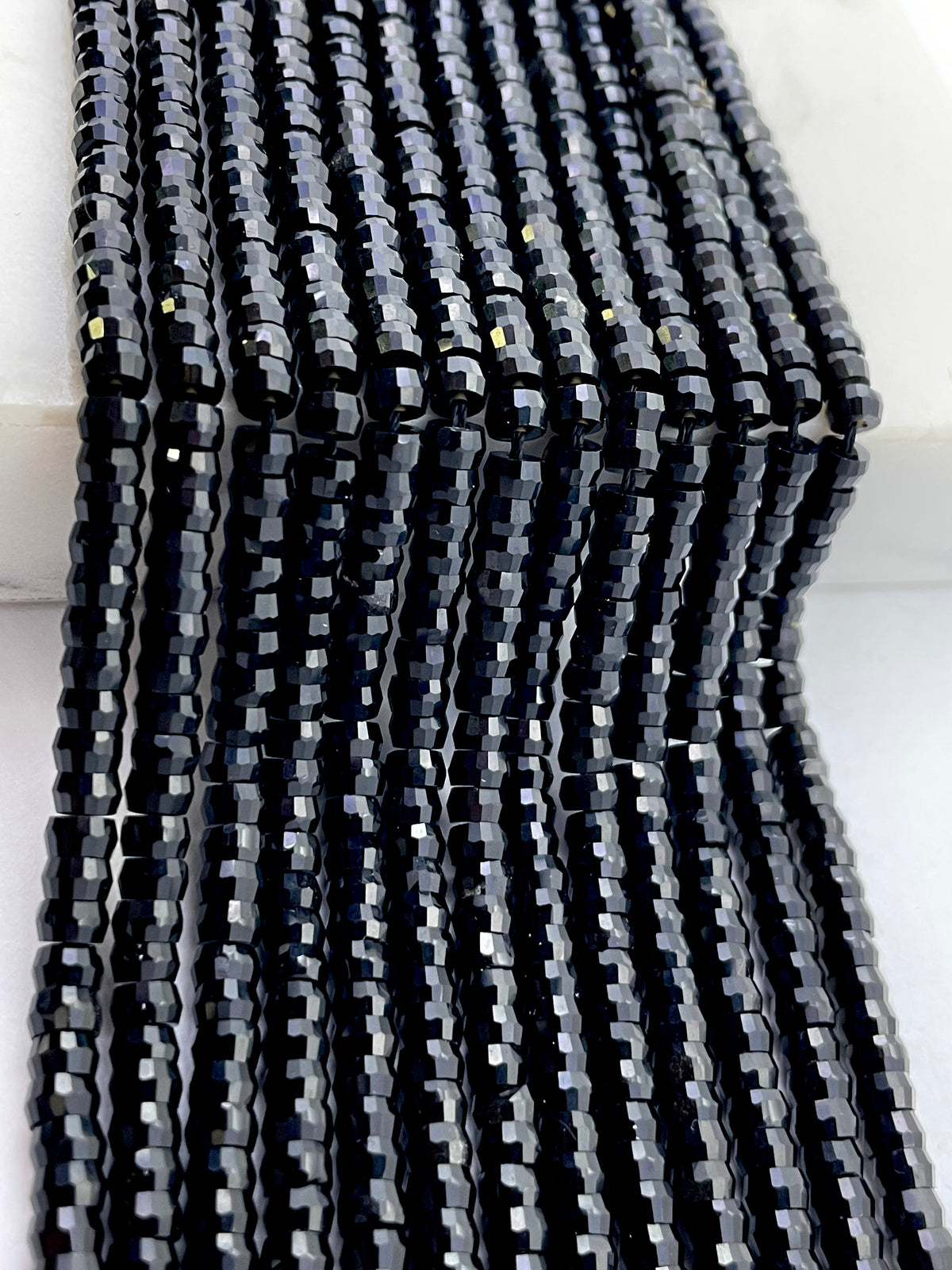 Multiple strands of faceted black onyx beads arranged vertically, showing their glossy, reflective surfaces on a white background.