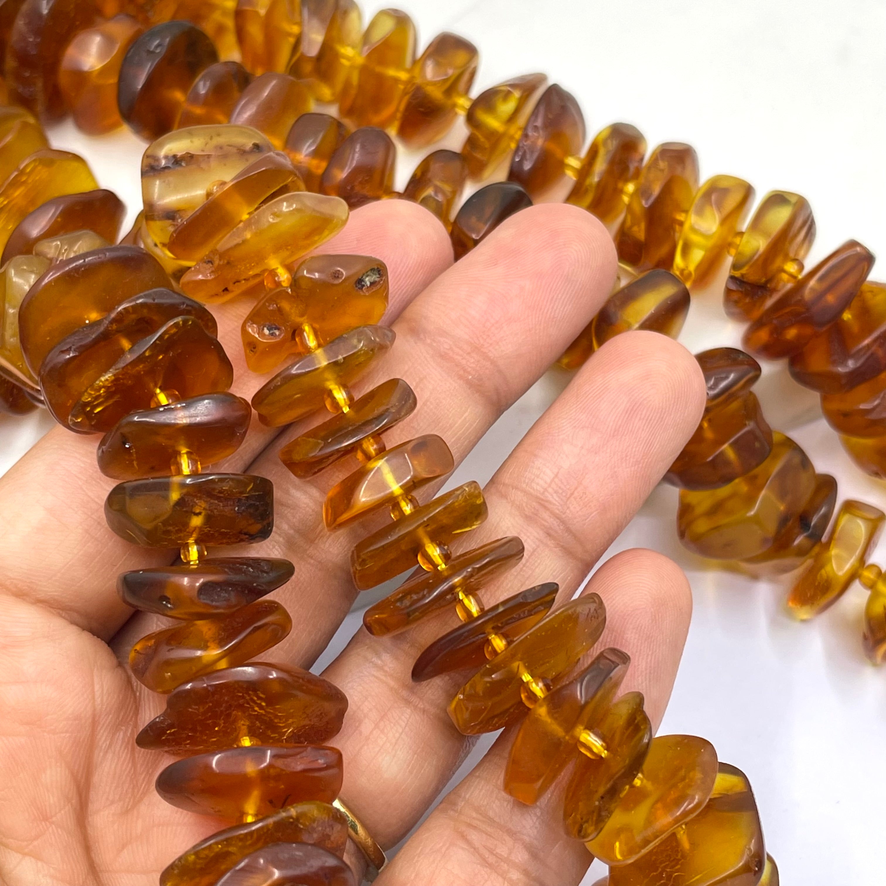 Chunky polished amber beads in a natural honey-brown color, shown draped over a person's hand to display their size and shape.