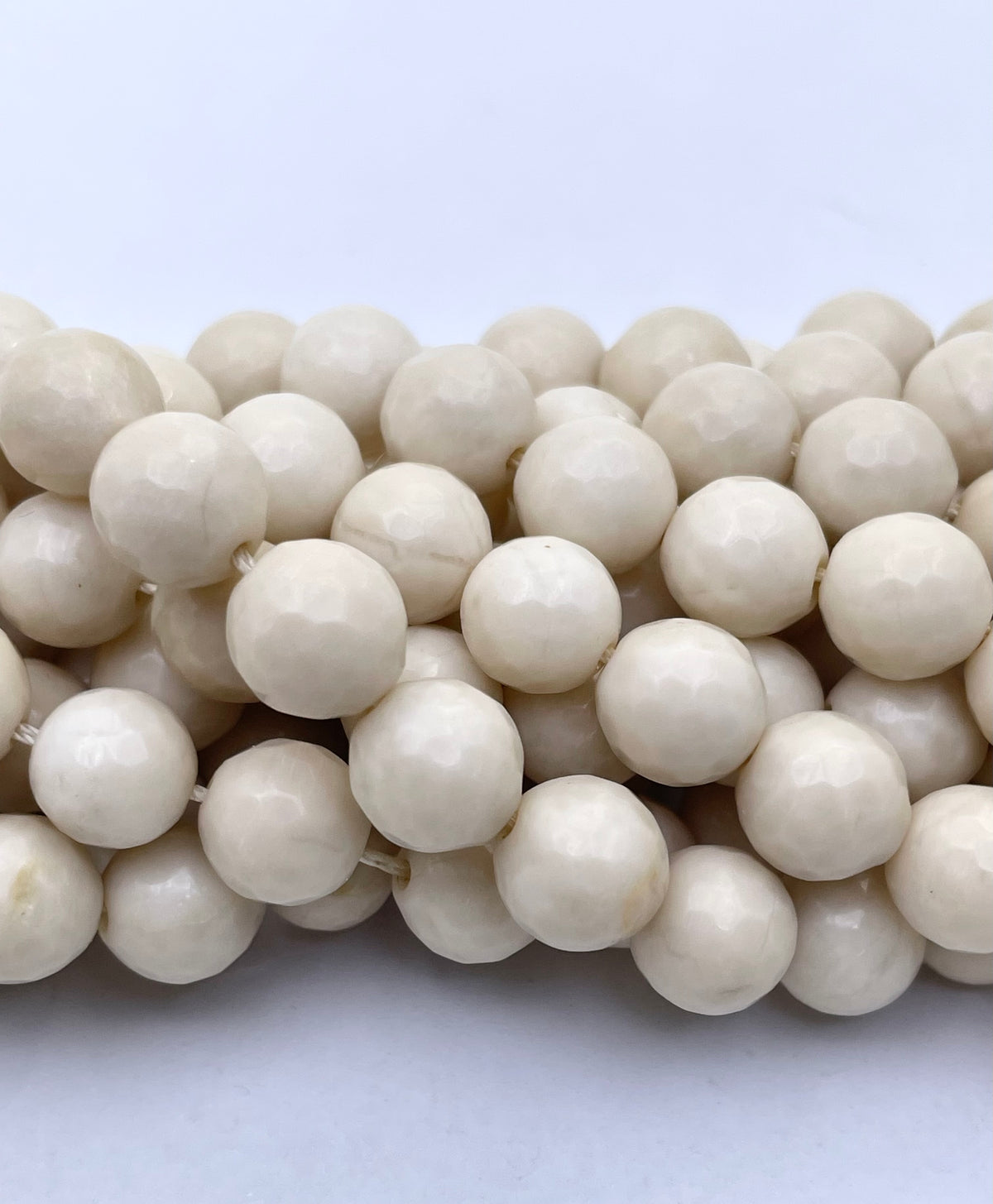 A close-up of multiple strands of faceted round fossil stone beads in a warm ivory or cream color, arranged horizontally against a plain light background.