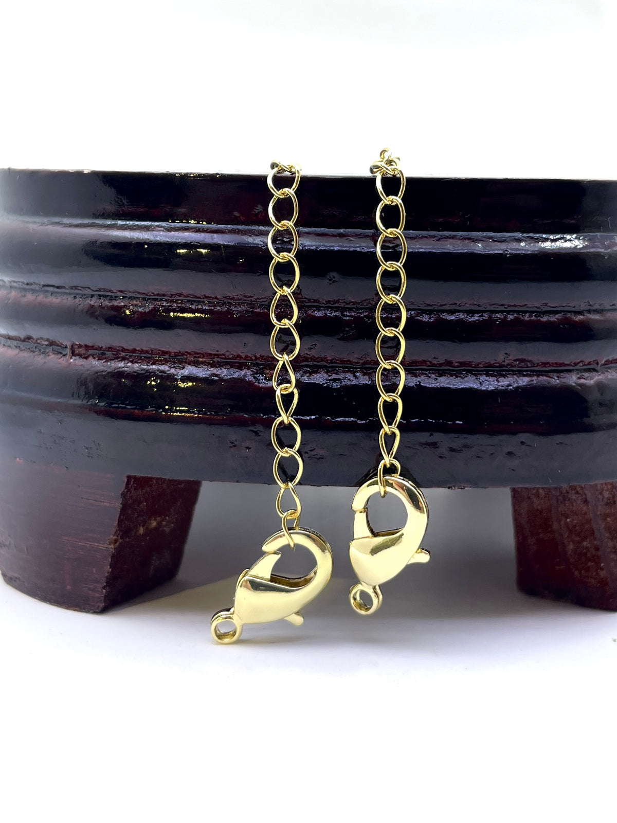 Two gold lobster claw clasp jump rings on a delicate chain, displayed against a dark wooden stand on a white background.
