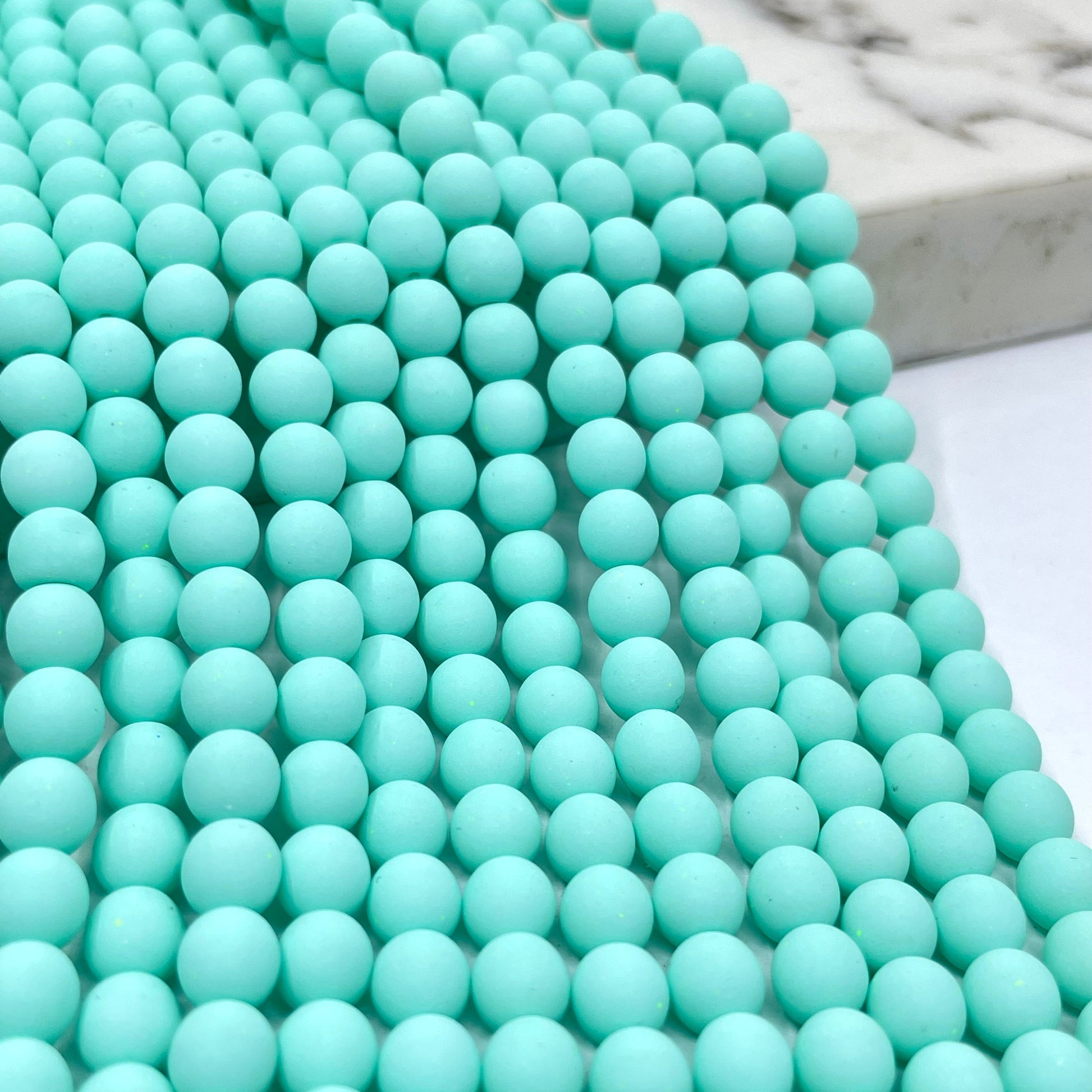 A close-up of seafoam blue velvet beads arranged in rows, with a marble-like surface visible in the background.