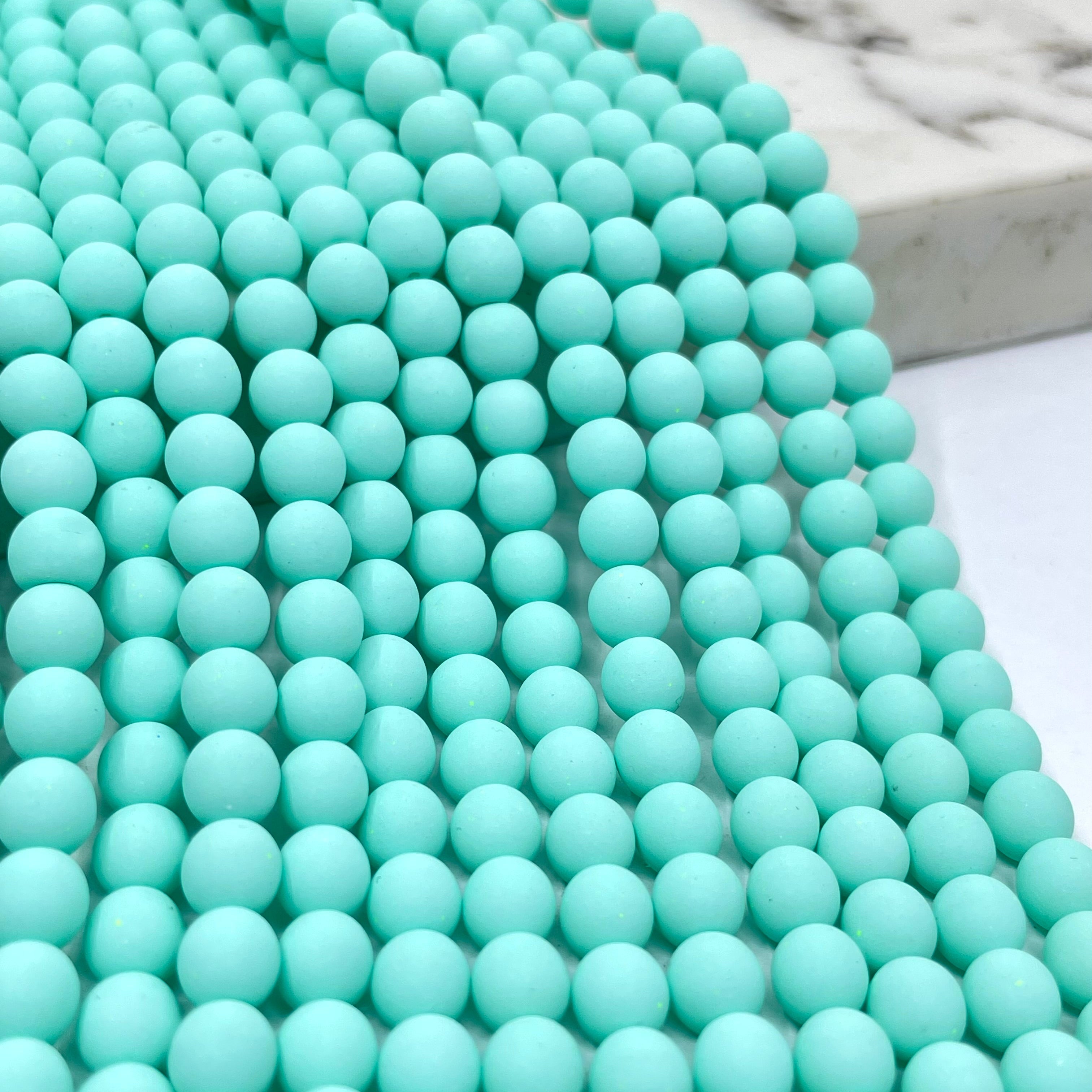 A close-up of seafoam blue velvet beads arranged in rows, with a marble-like surface visible in the background.