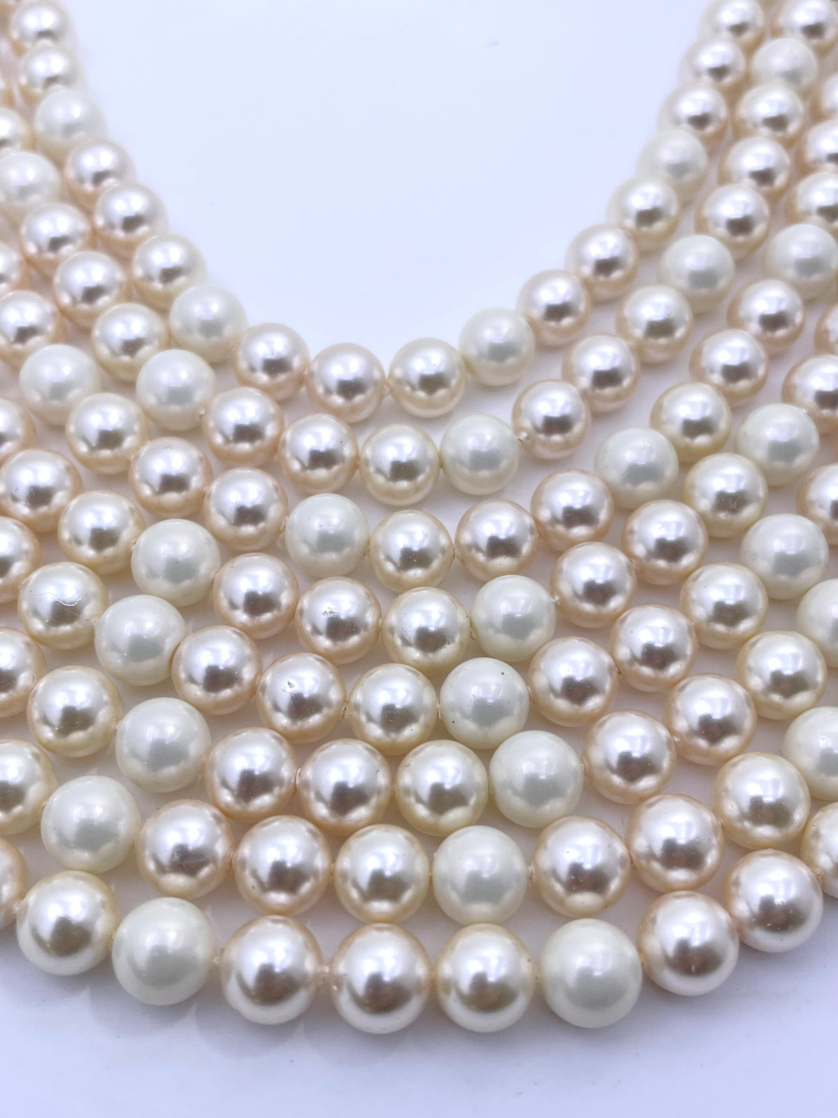 Multiple strands of round shell pearl beads in an off-white, creamy color, arranged in parallel rows on a plain white background.