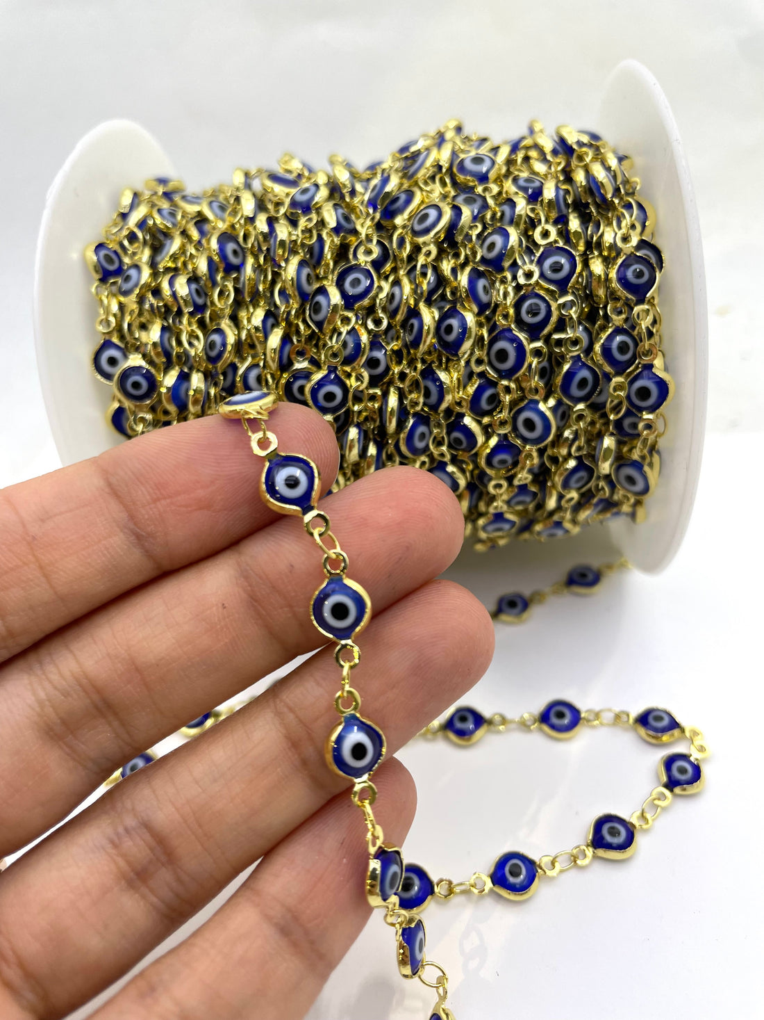 Gold chain with blue evil eye, shown spool-wrapped and draped on a white surface.