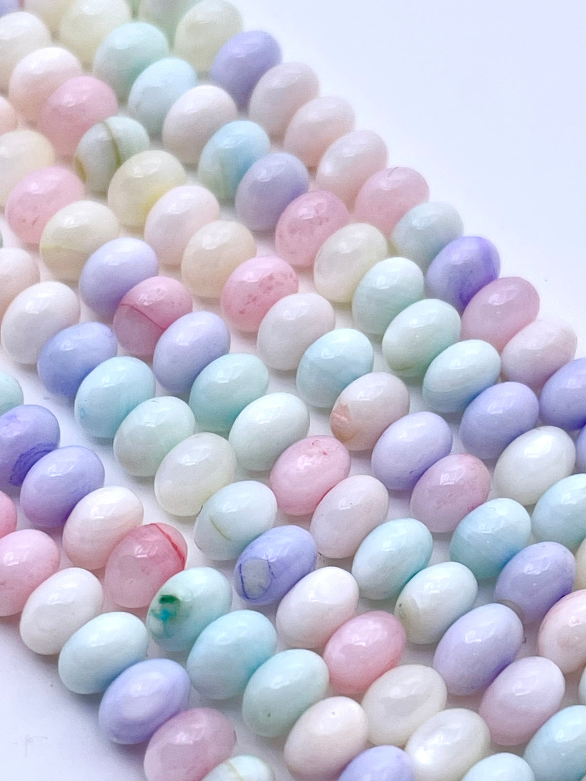 Faceted pastel mop beads in multiple colors including pink, blue, purple, and green, arranged in diagonal rows on a white background.
