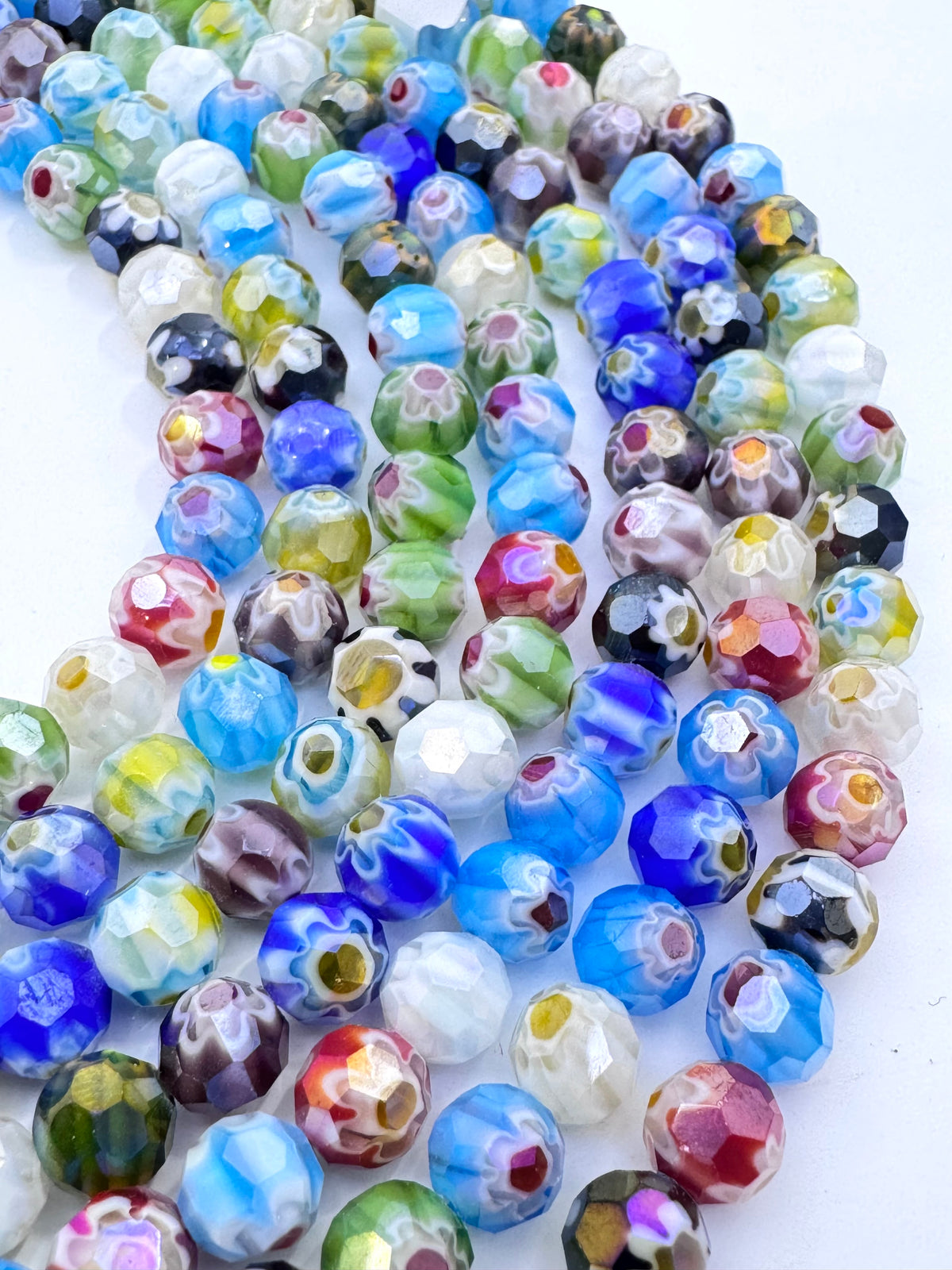 A close-up of multiple strands of faceted glass beads in a multicolor marbled pattern, including blue, green, white, purple, red, and yellow, arranged on a plain white background.