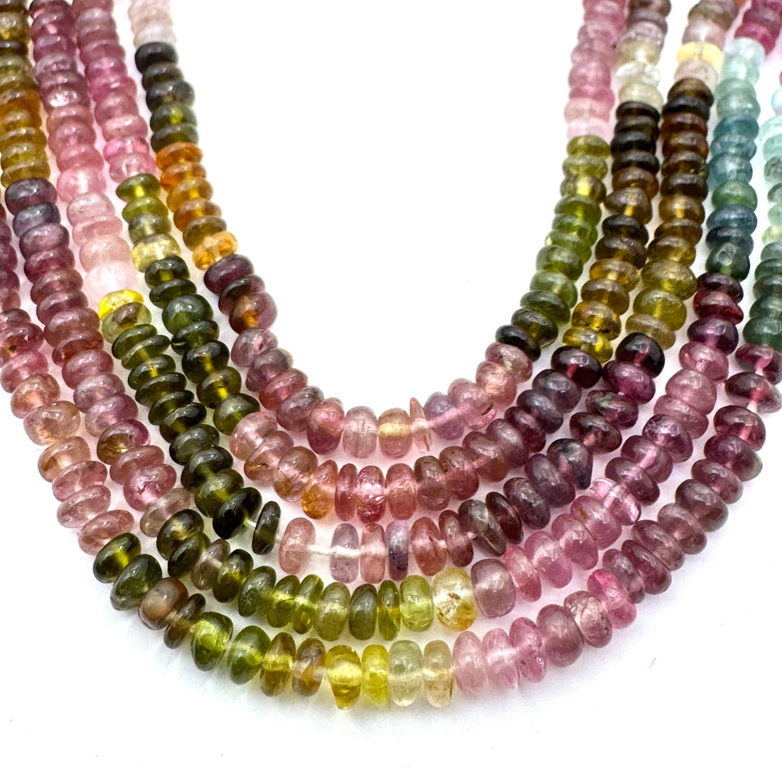 Multiple strands of smooth rondelle mix tourmaline gemstone beads in assorted colors including pink, green, yellow, purple, and brown, arranged in curved rows on a white background.