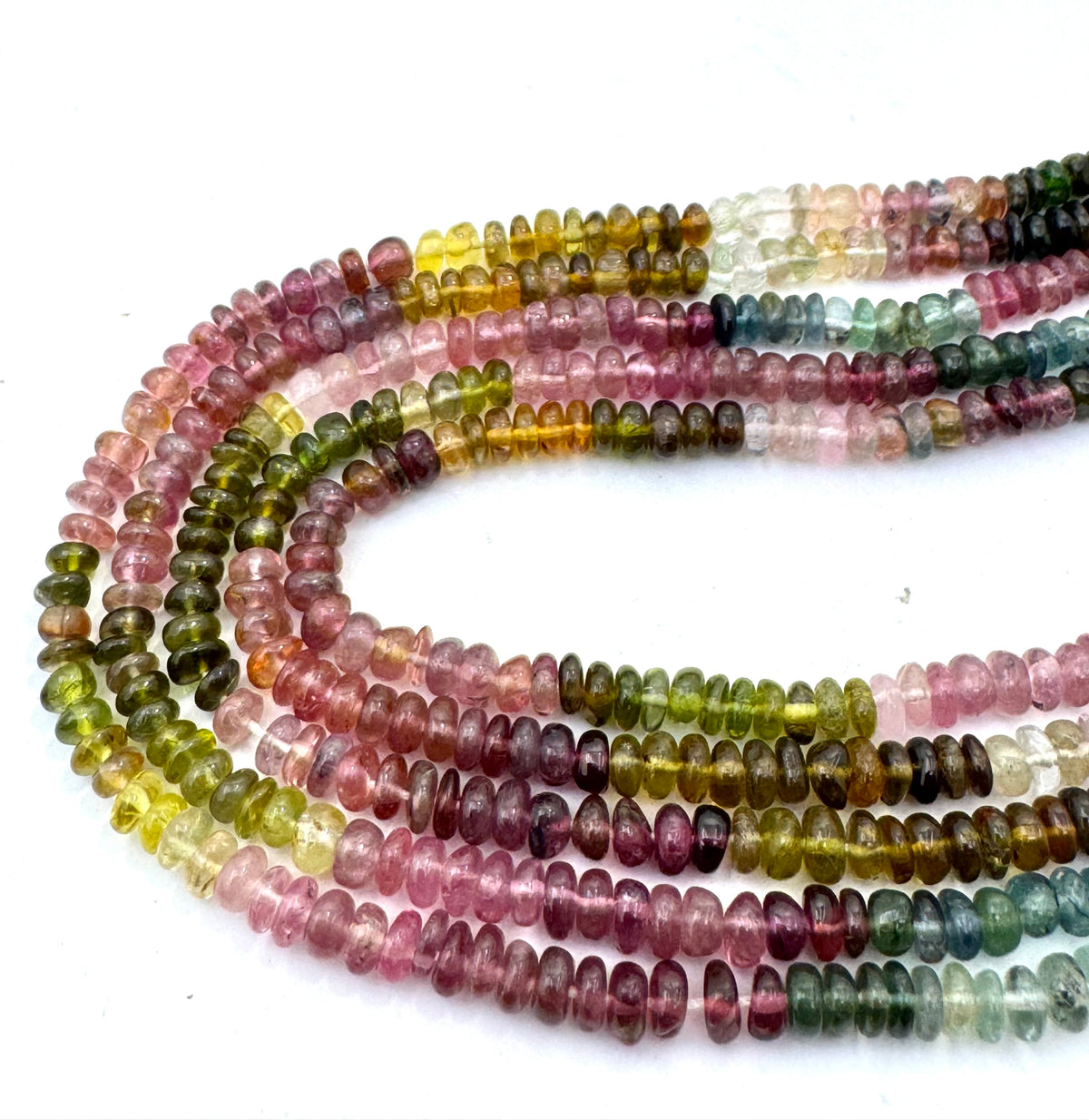 Multiple strands of small disc mix tourmaline beads in assorted translucent colors including pink, green, yellow, blue, and purple, arranged on a plain white background.