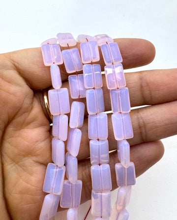 A hand holding a strand of pink opalite translucent rectangular beads, shown against a plain white background.