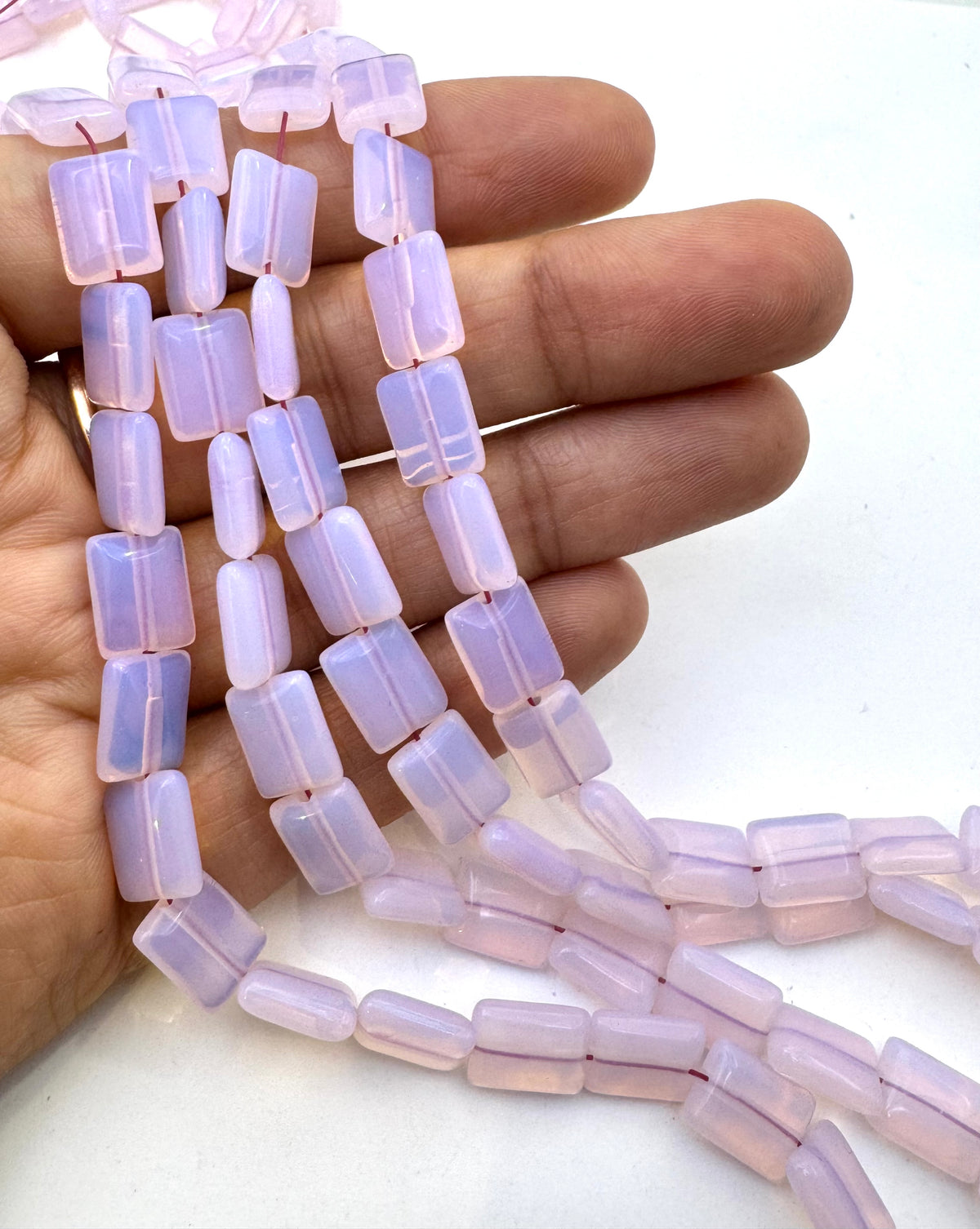 Light pink translucent rectangular opalite beads strung on cords, held in a person's hand against a plain white background.