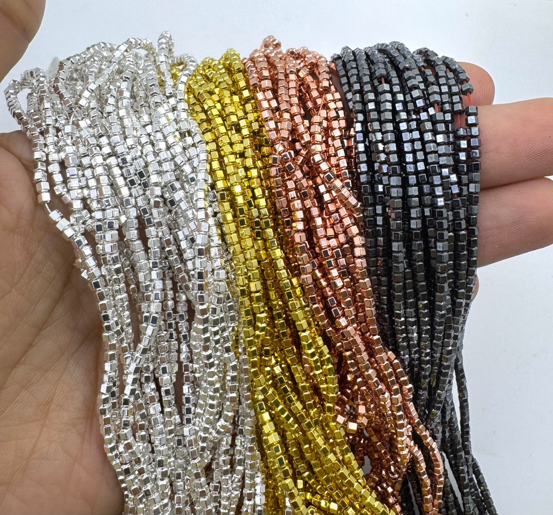 Three strands of mini hematite beads held in a hand, showing silver, gold, and rose gold metallic colors against a plain white background.