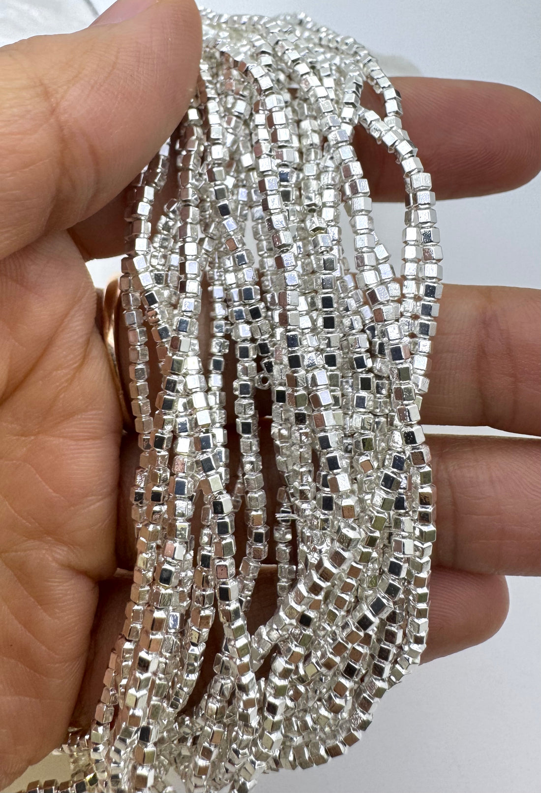 Three strands of mini hematite beads held in a hand, showing silver, gold, and rose gold metallic colors against a plain white background.