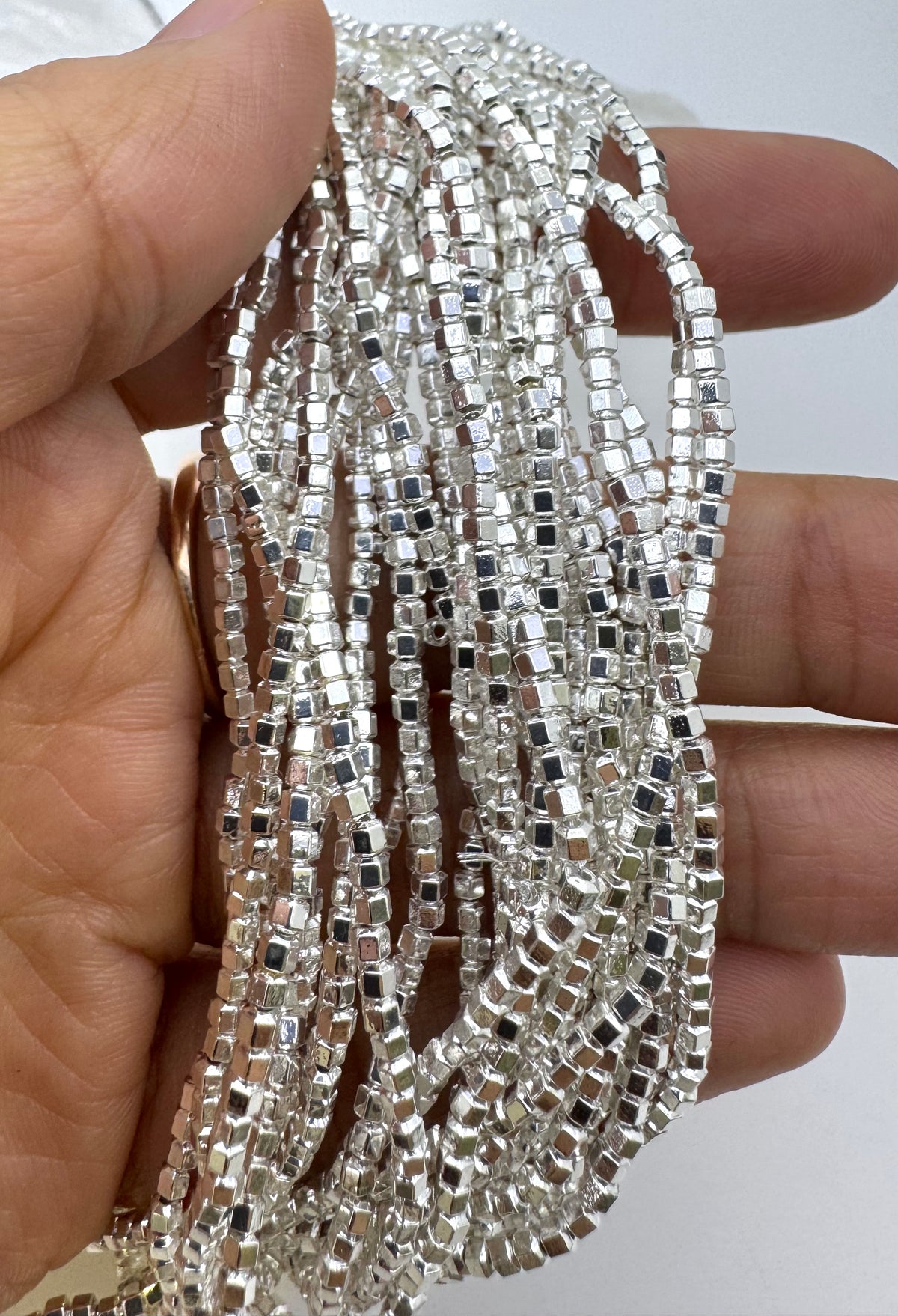 A hand holding a bundle of long strands of small silver hematite beads.