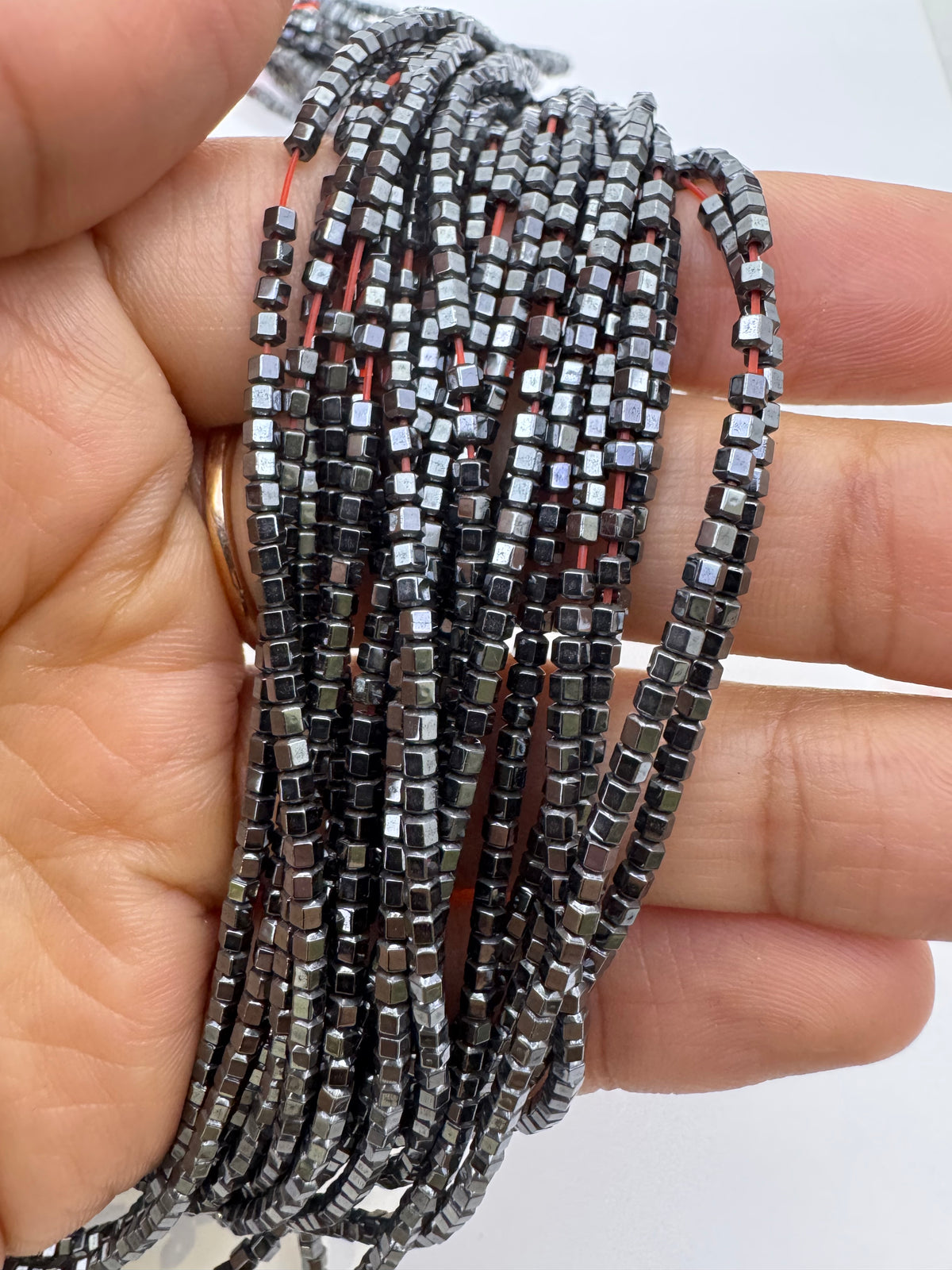 A hand holding a bundle of multiple strands of small natural hematite beads