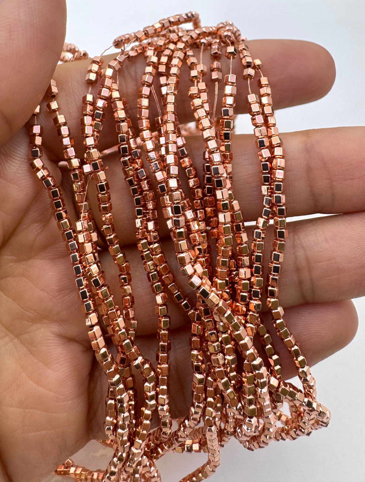 A hand holding a bundle of rose gold hematite beads