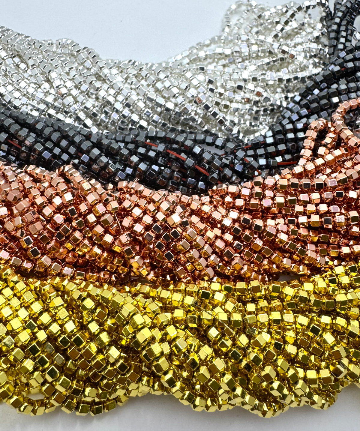 Close-up of multiple strands of gold, rose gold, gunmetal and silver hematite polyhedron beads