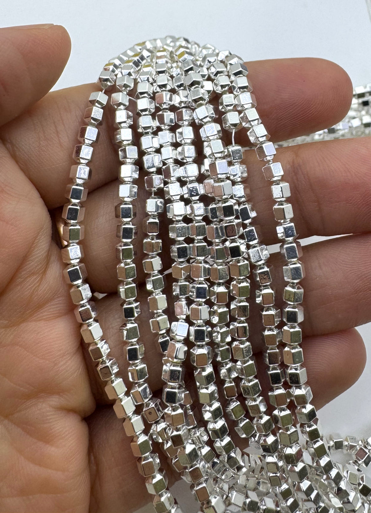 A close-up of a hand holding several strands of small, faceted silver hematite beads