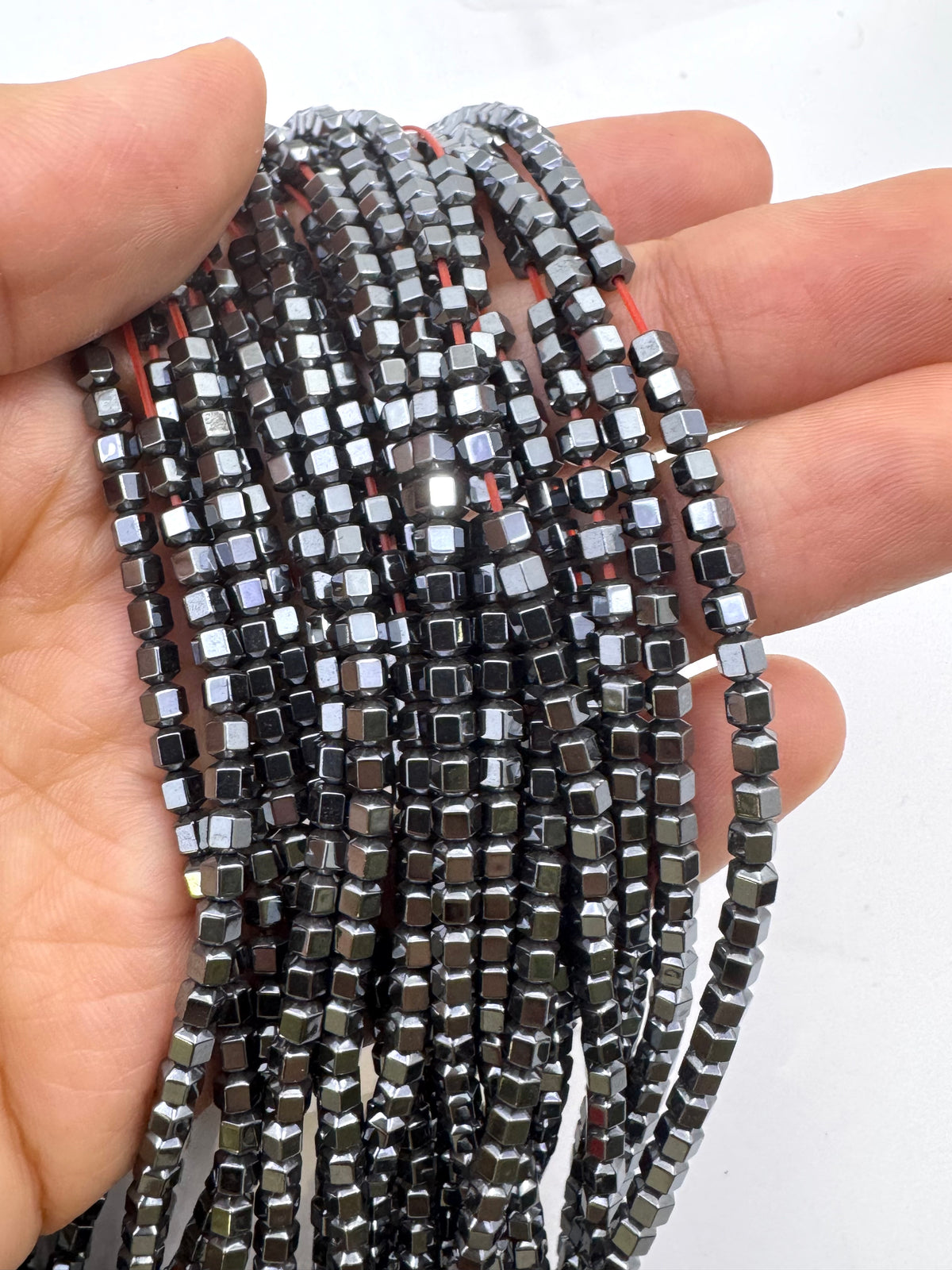 A hand holding several strands of small natural hematite beads