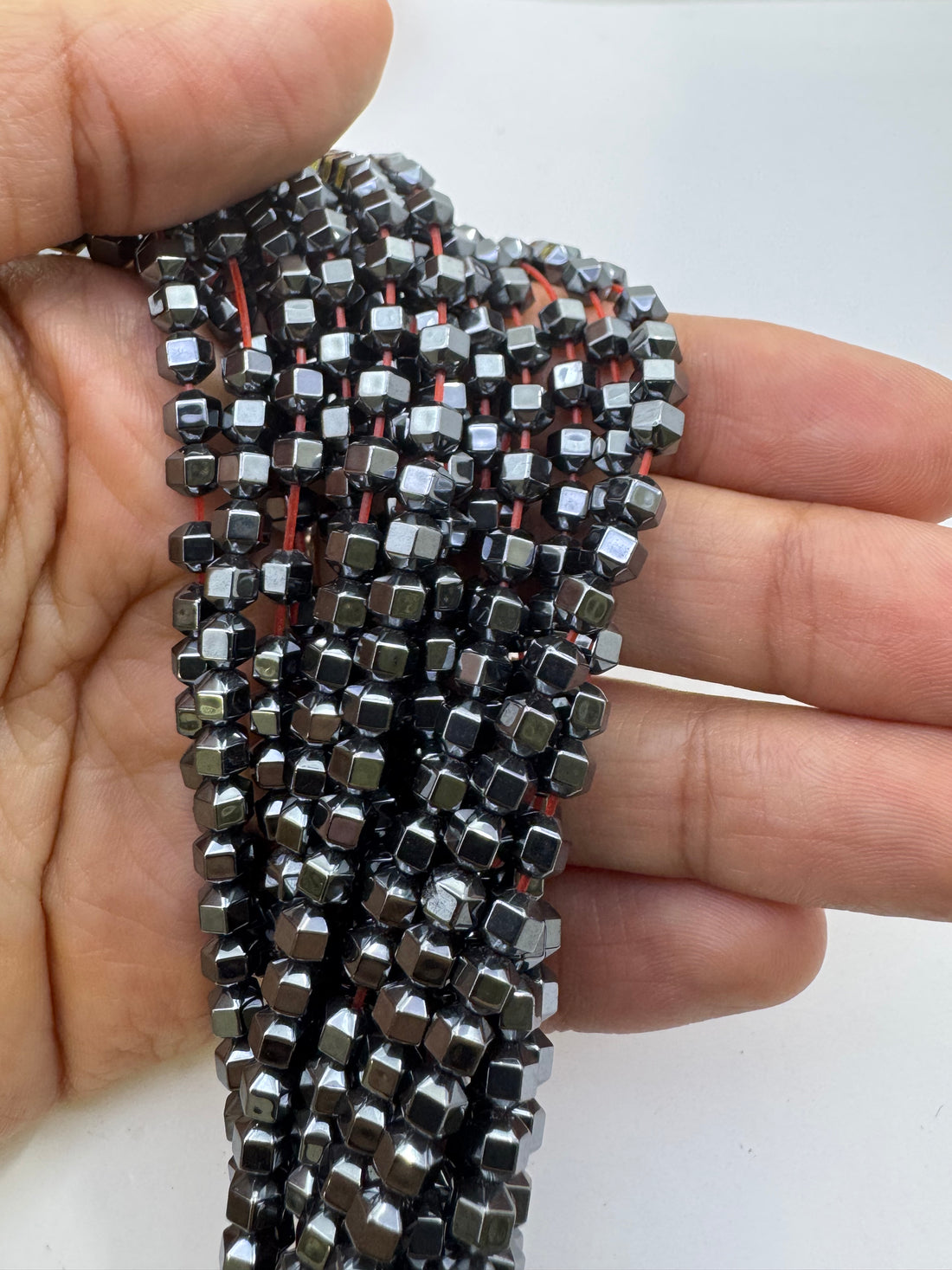 Multiple strands of metallic hematite beads arranged in horizontal rows, showing silver, rose gold, yellow gold, and gunmetal gray colors.