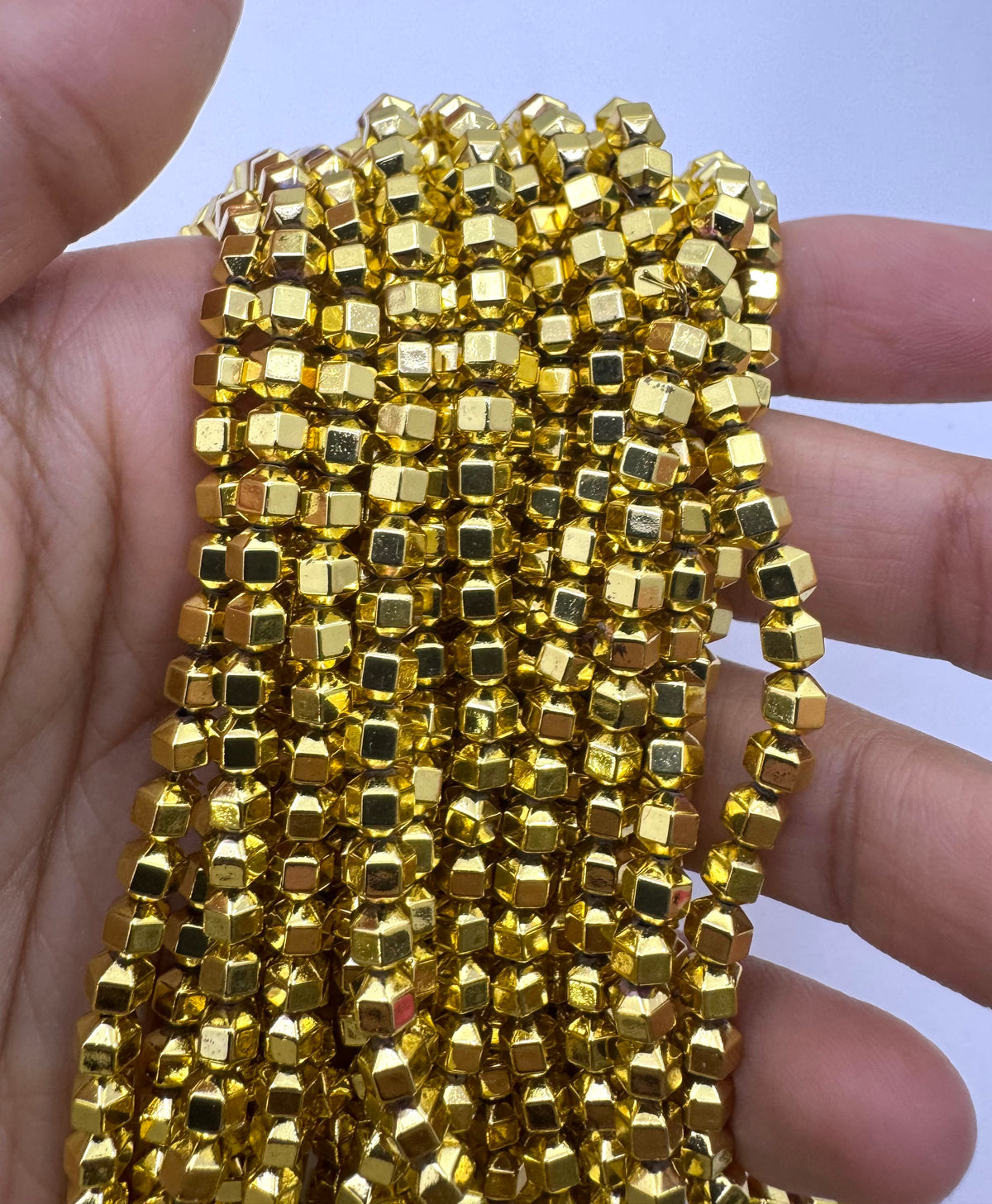 A hand holding a bundle of shiny gold hematite beads