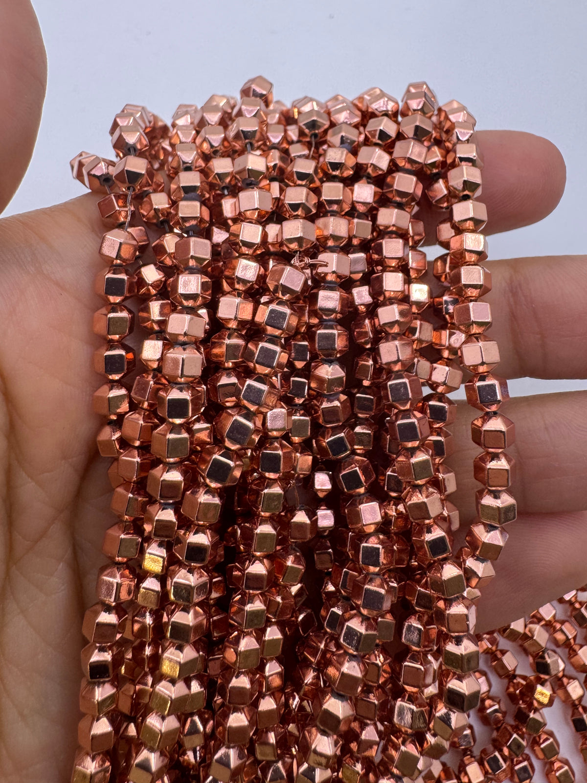 A hand holding multiple strands of metallic rose gold hematite beads