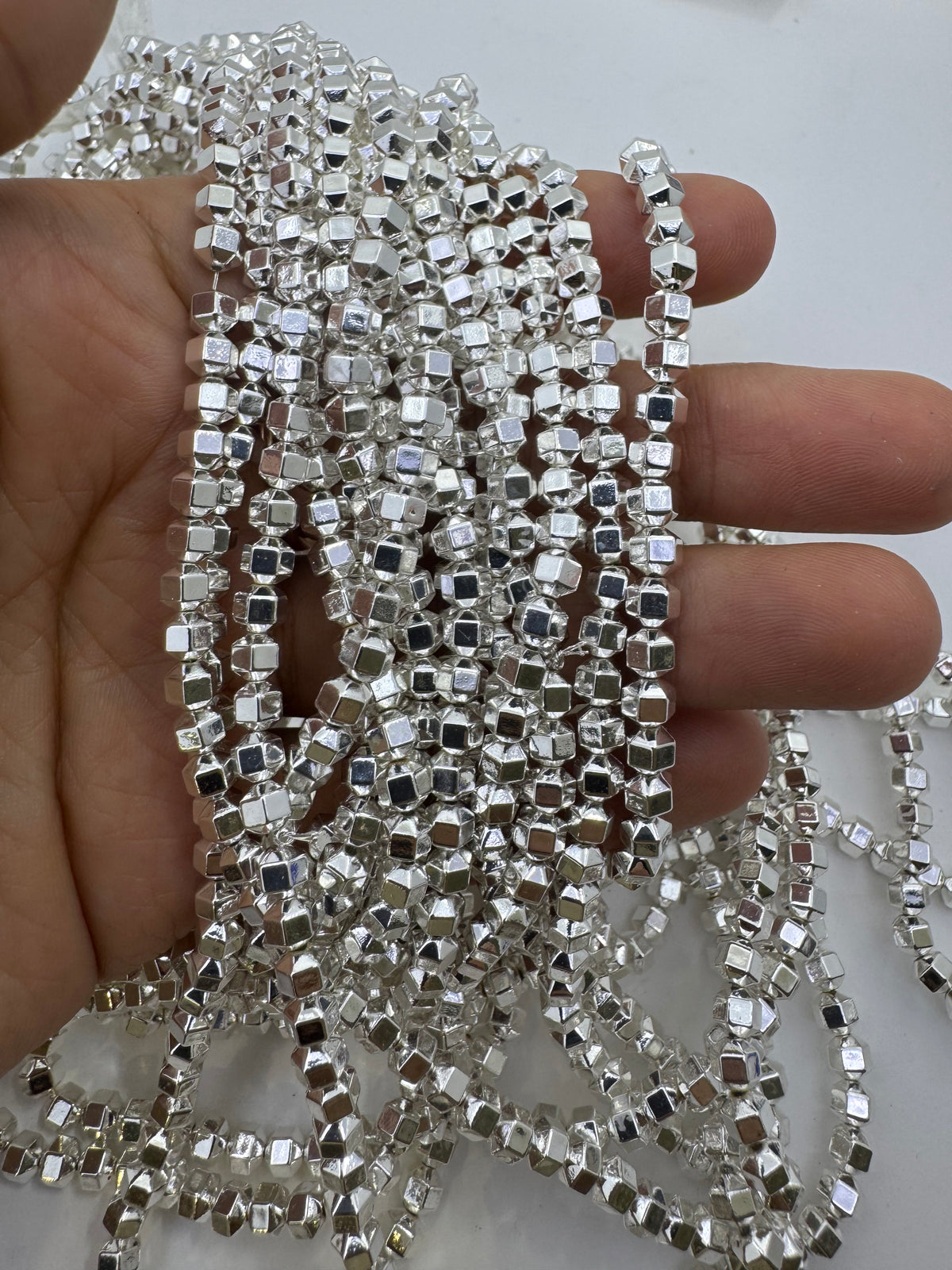 A hand holding a bundle of long strands of small silver hematite beads