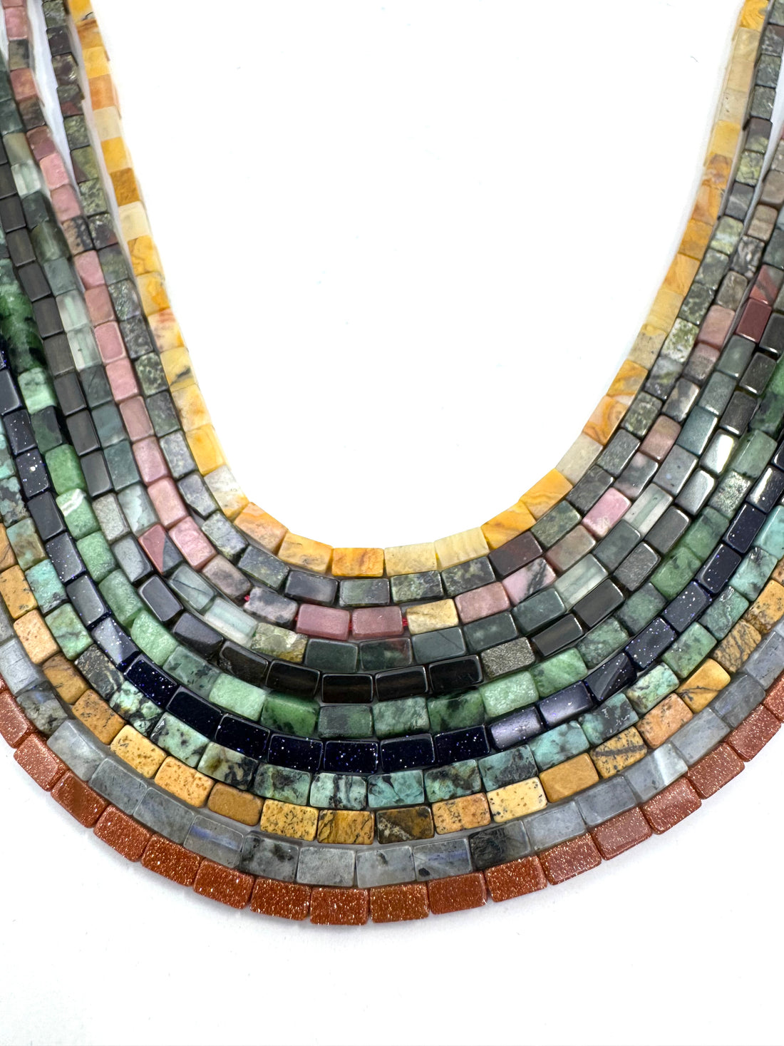 Curved strands of rectangular gemstone beads in multiple colors, including green, blue, pink, yellow, orange, and black, arranged on a plain white background.