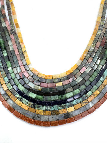 Curved strands of rectangular gemstone beads in multiple colors, including green, blue, pink, yellow, orange, and black, arranged on a plain white background.